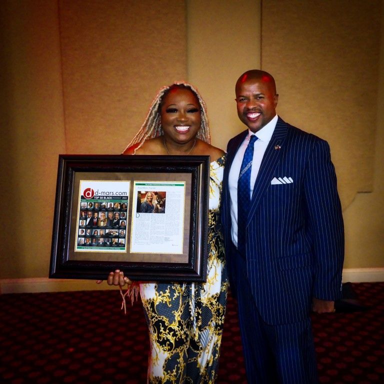 A man in a suit and tie stands next to a woman holding a framed picture