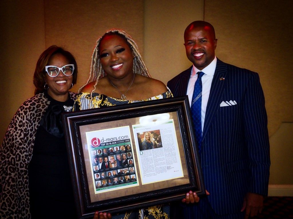 A man and two women are standing next to each other holding a framed picture.