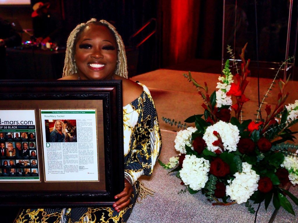 A woman is holding a framed picture in front of flowers.