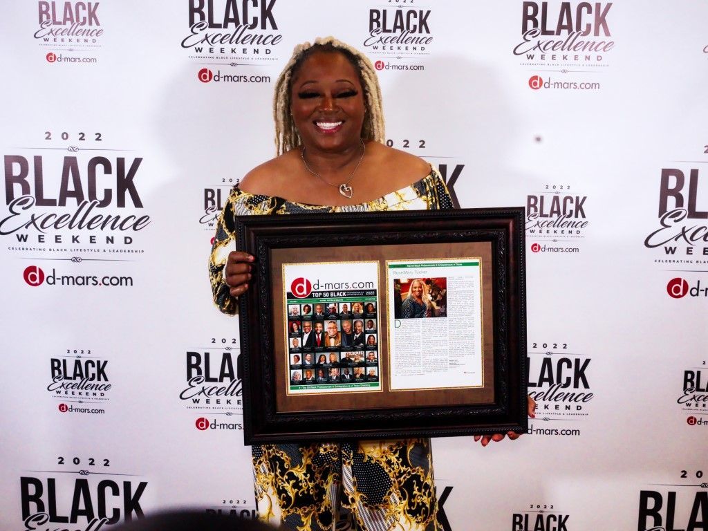 A woman is holding a framed picture in front of a wall that says black excellence