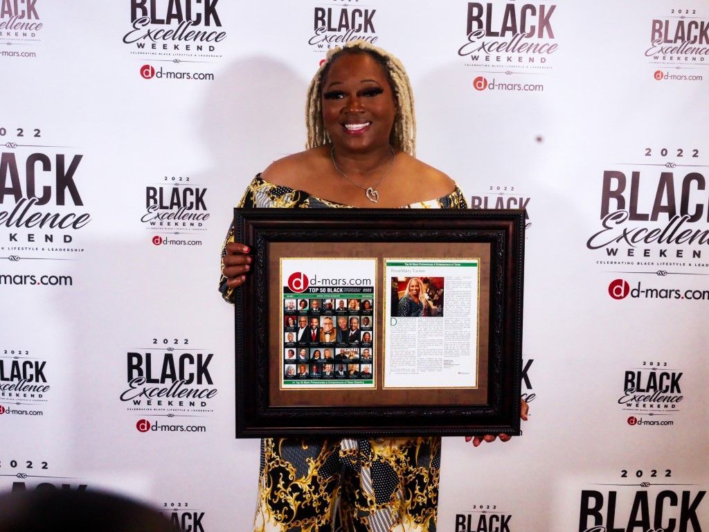 A woman is holding a framed picture in front of a black wall.