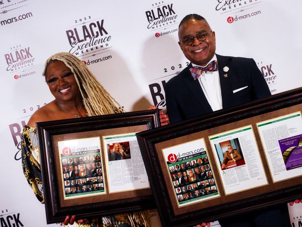 A man and a woman are holding framed pictures on a red carpet.