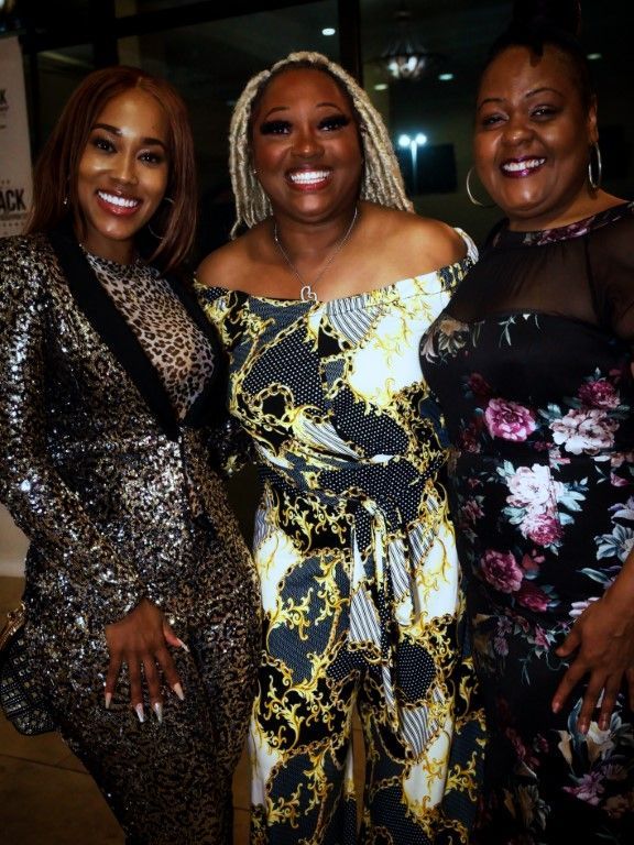 Three women posing for a picture with one wearing a floral dress