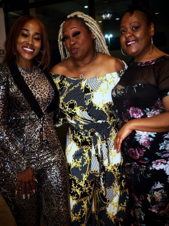 Three women posing for a picture with one wearing a leopard print jumpsuit