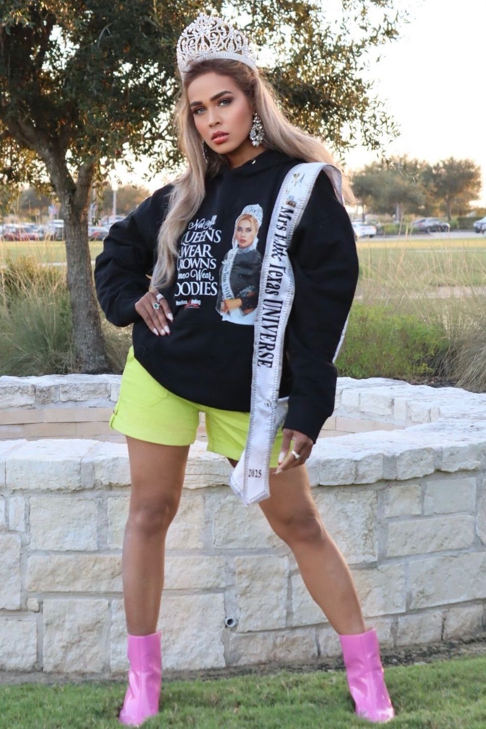 A woman wearing a black hoodie and neon yellow shorts is holding a sash.