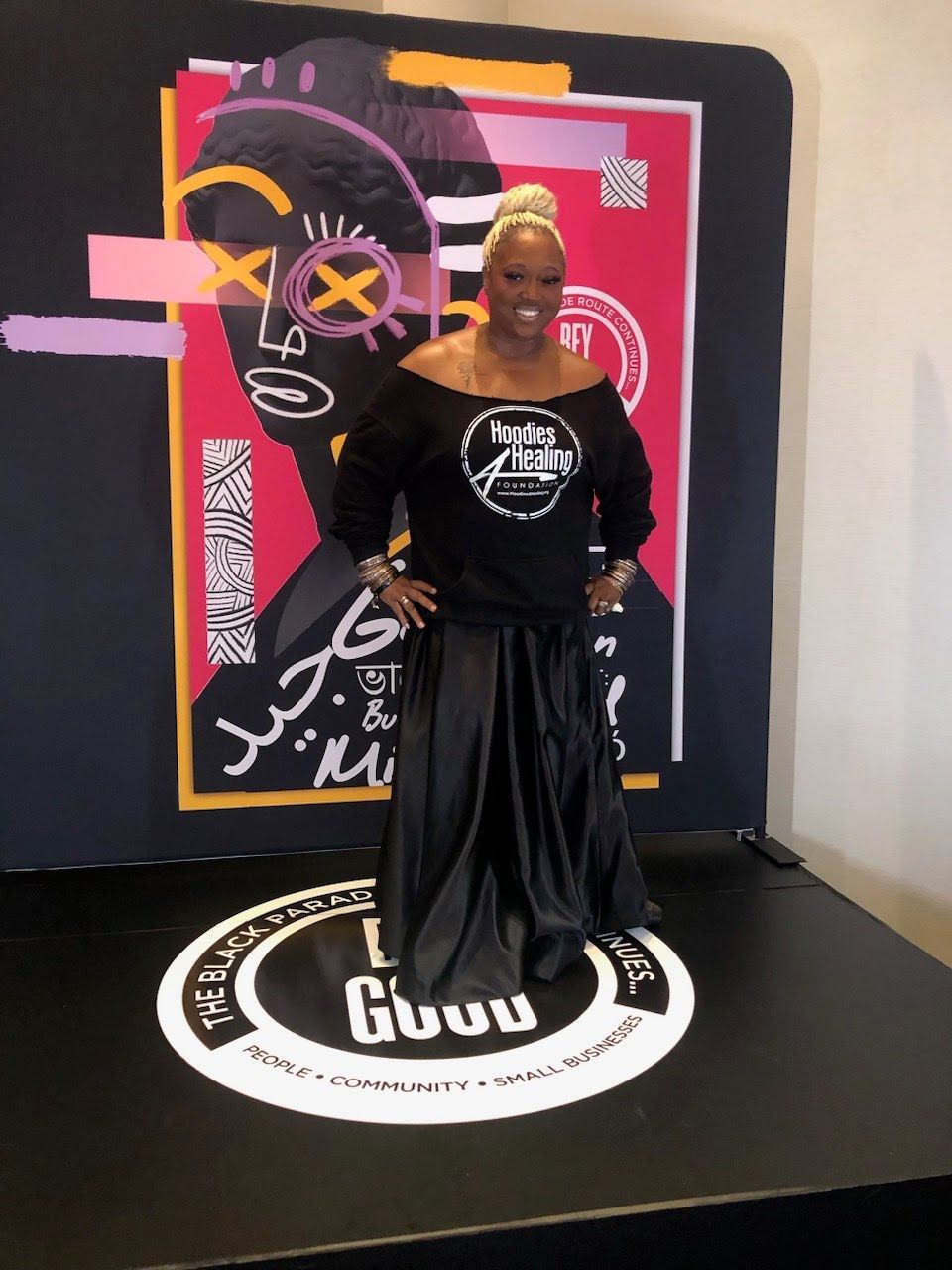 A woman in a black dress is standing in front of a poster that says gugu