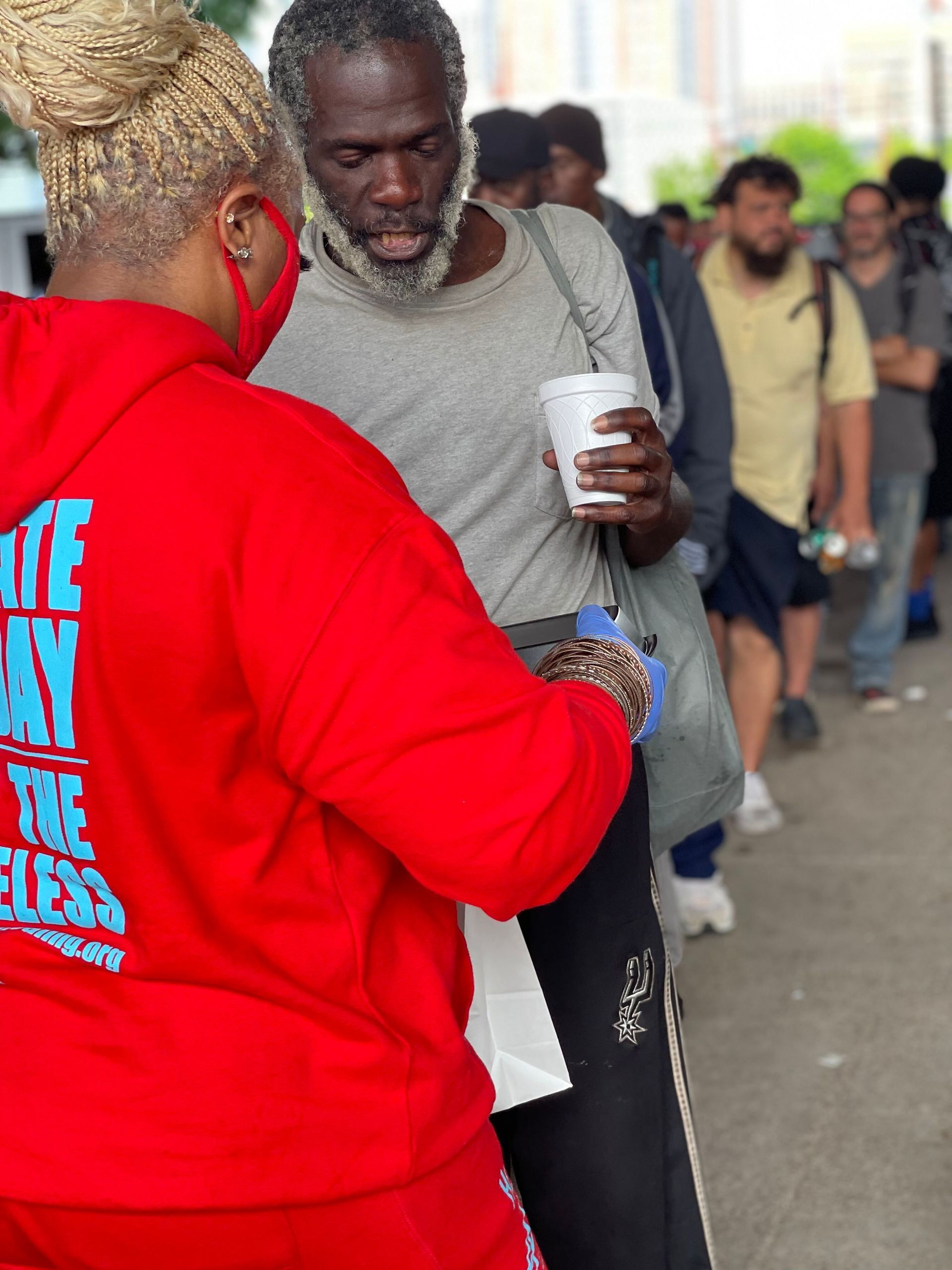 A woman in a red hoodie is helping a man with a cup of coffee