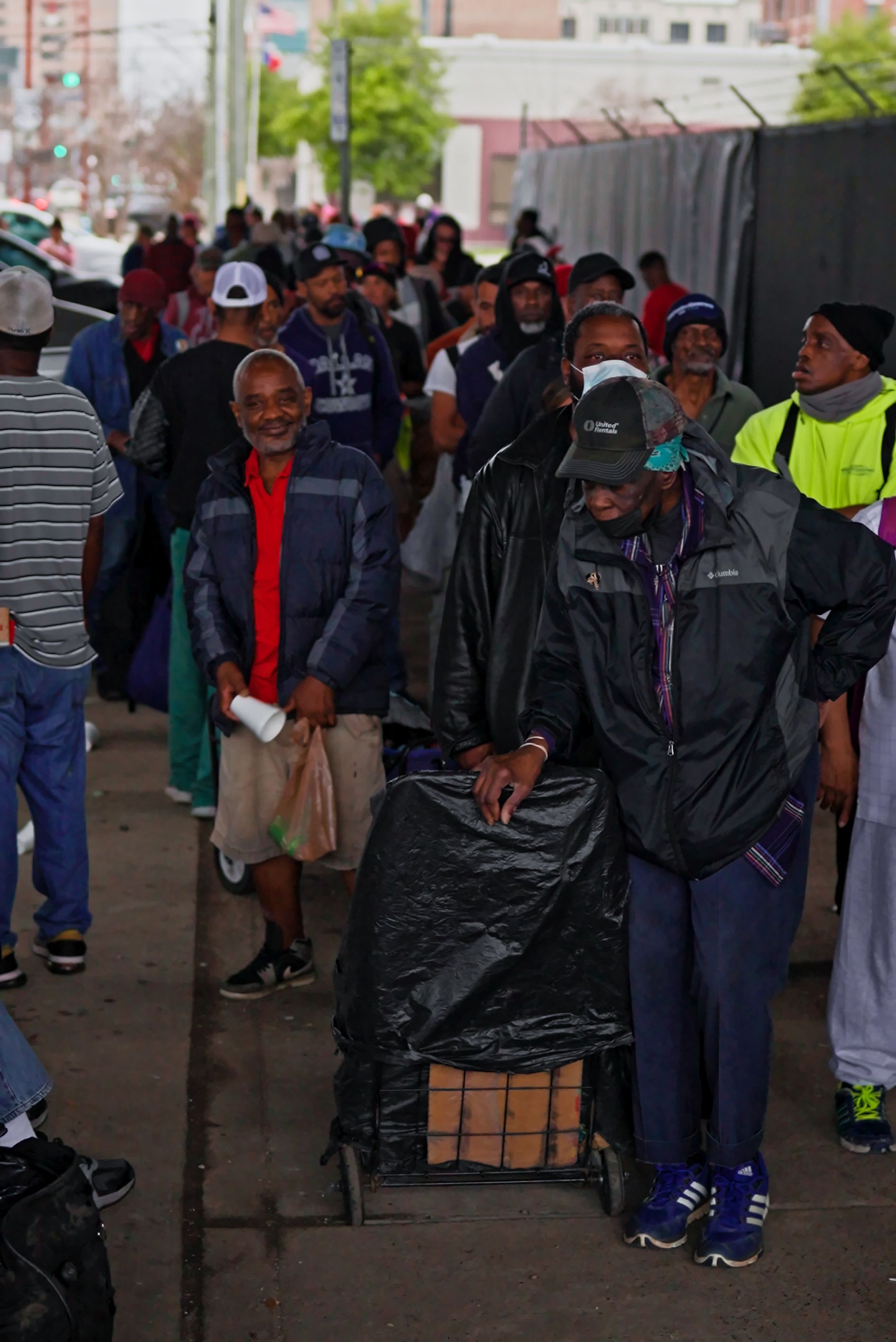 A group of people are standing in a line on the sidewalk.
