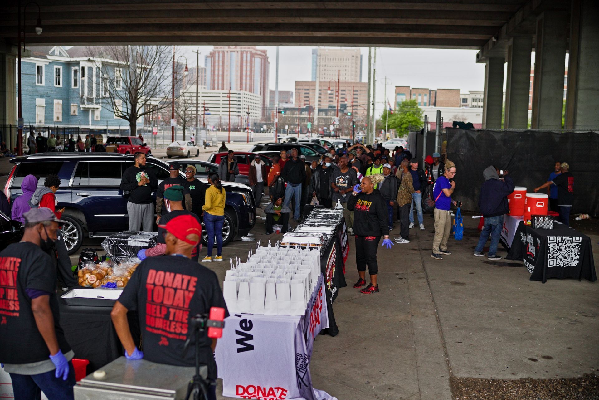 A group of people are standing around tables under a bridge.
