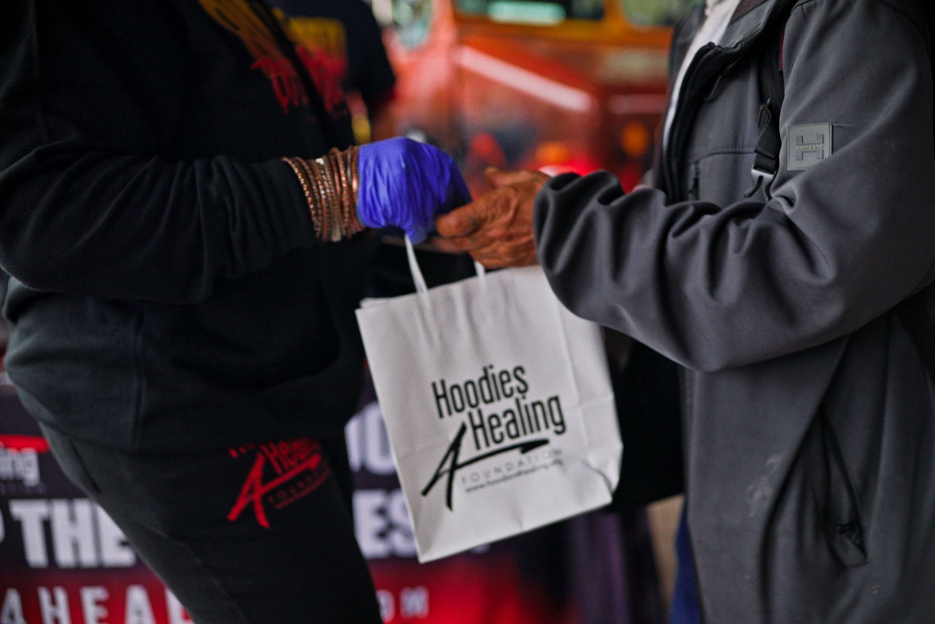 A person wearing purple gloves is handing a bag to another person.