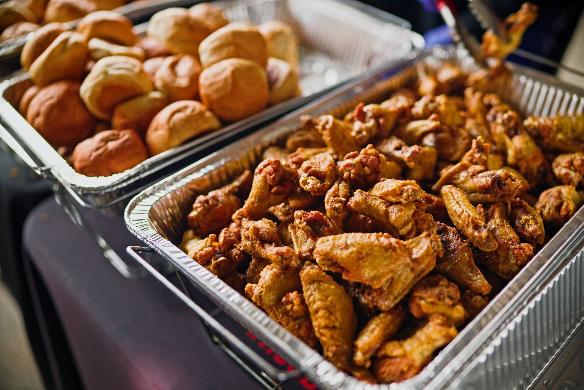 Two trays of fried chicken and rolls are sitting on a table.