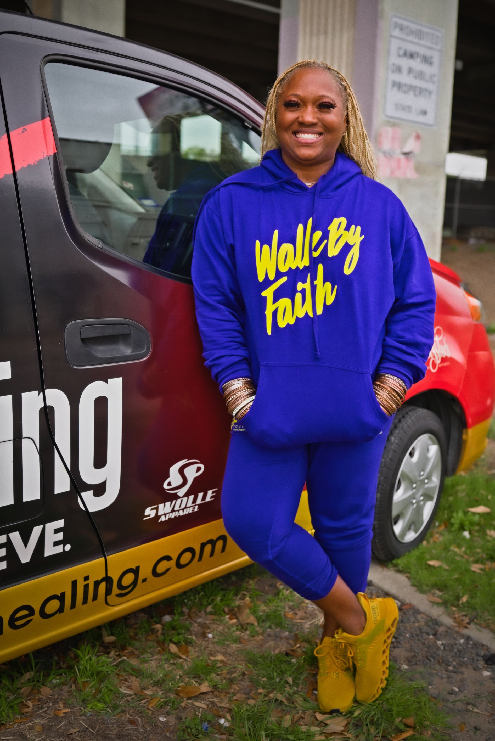 A woman in a blue hoodie is standing in front of a van.