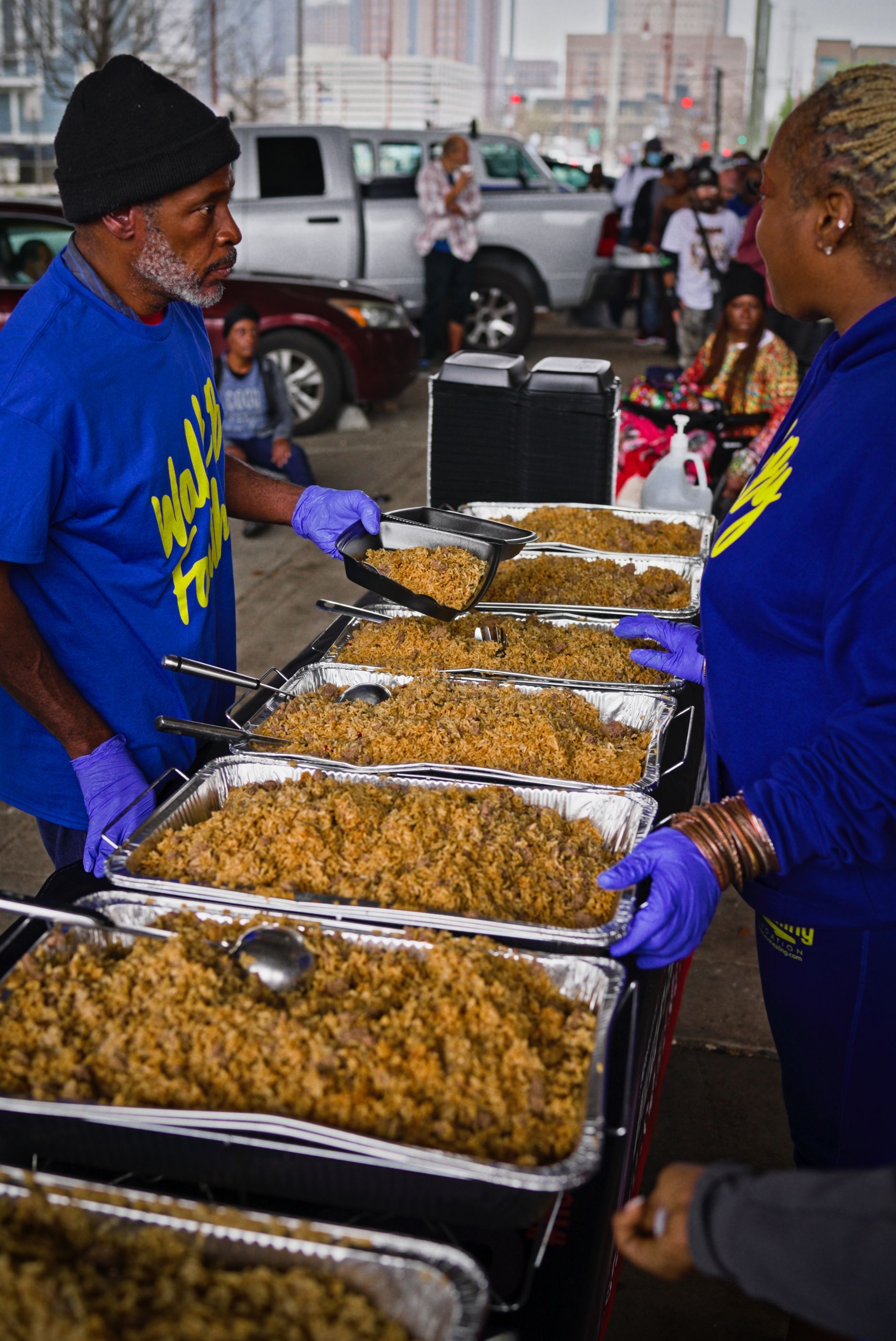 A man in a blue shirt is serving food to a woman in purple gloves.