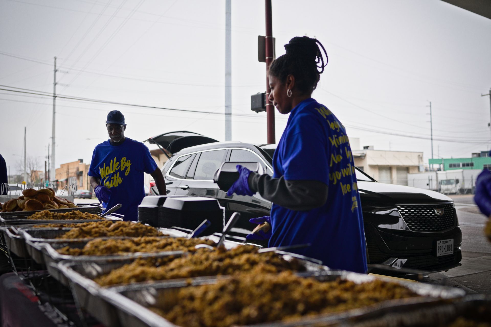 A woman in a blue shirt is standing in front of a table filled with trays of food.