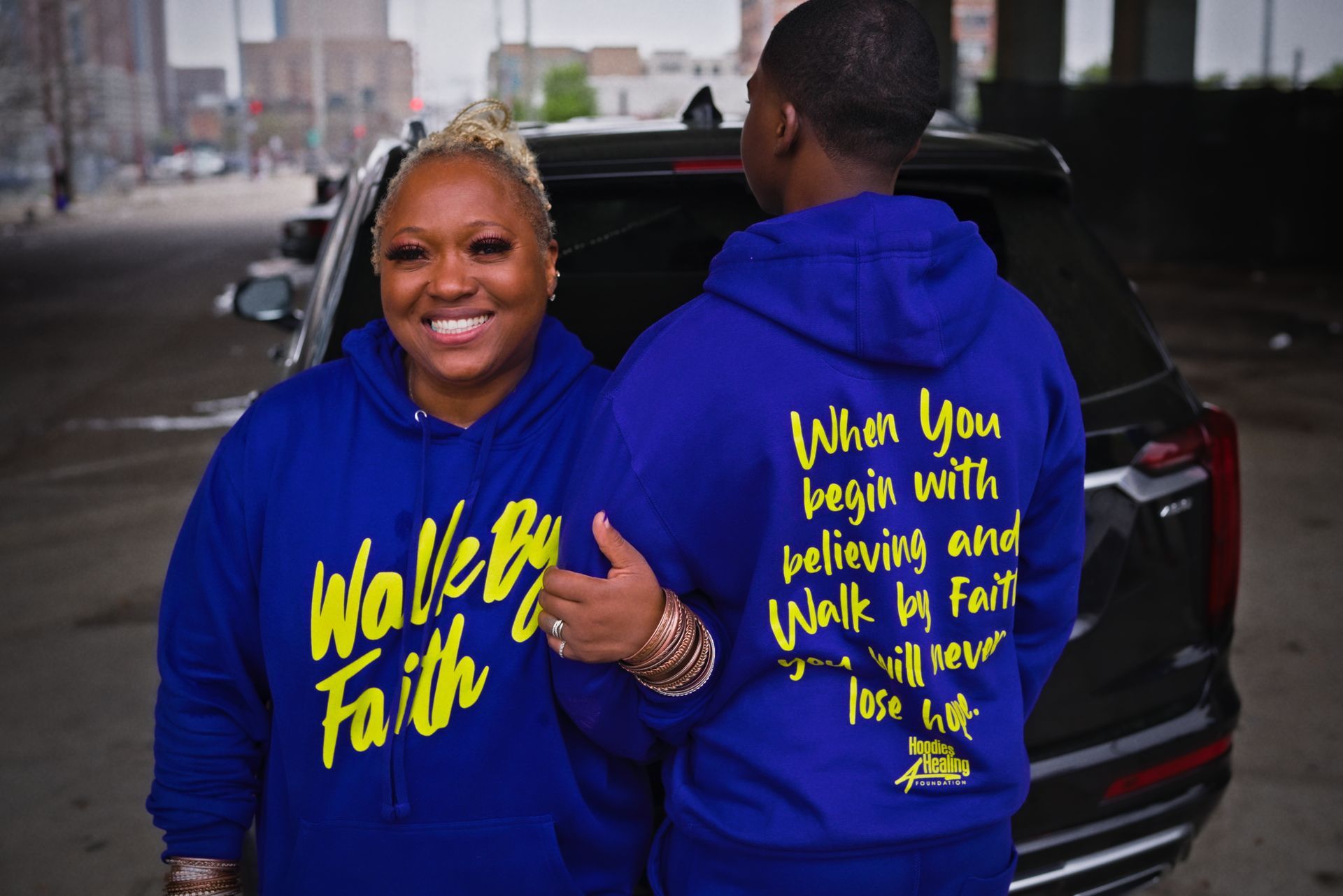 A man and woman wearing blue hoodies that say walk by faith