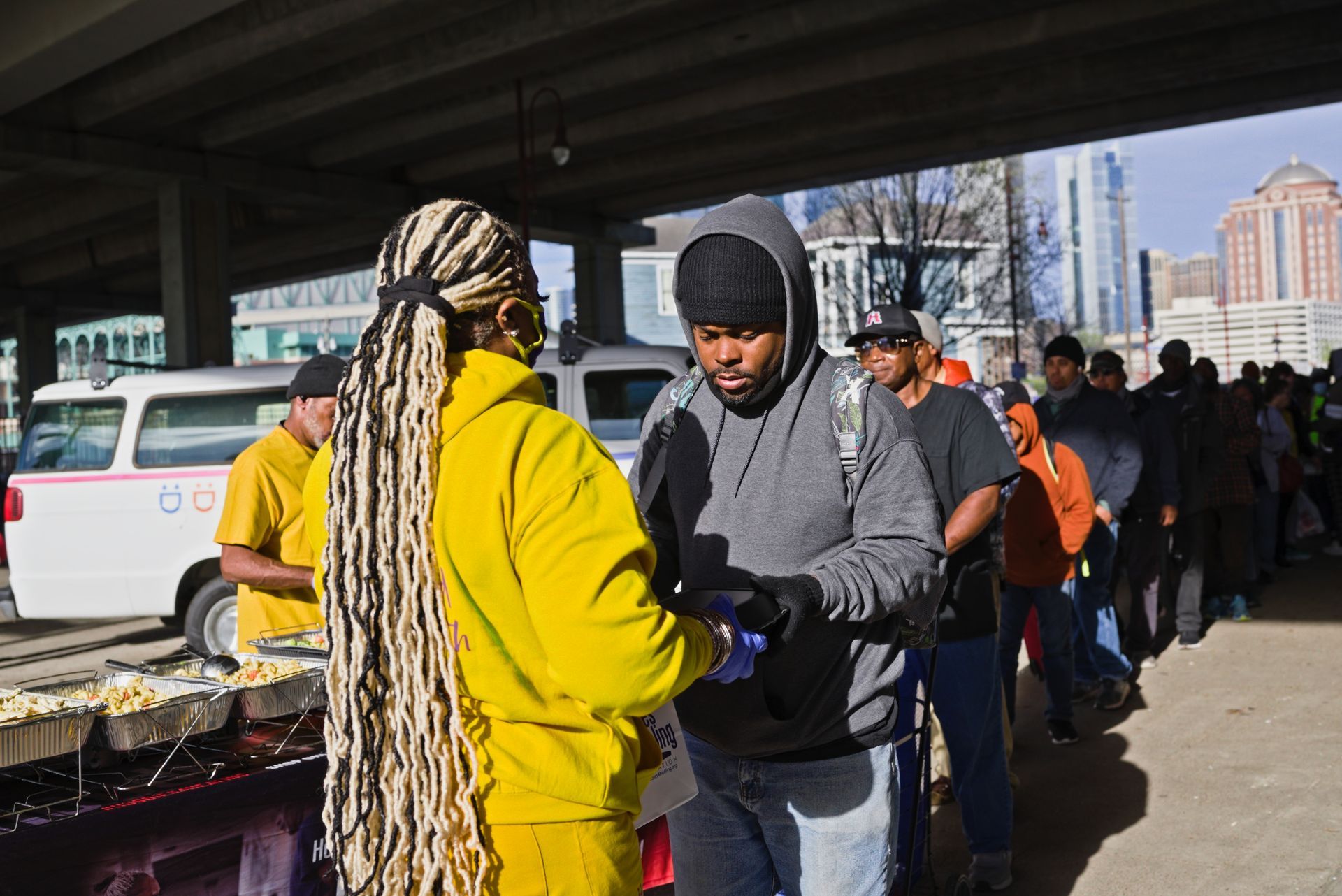 A group of people are standing in a line under a bridge.