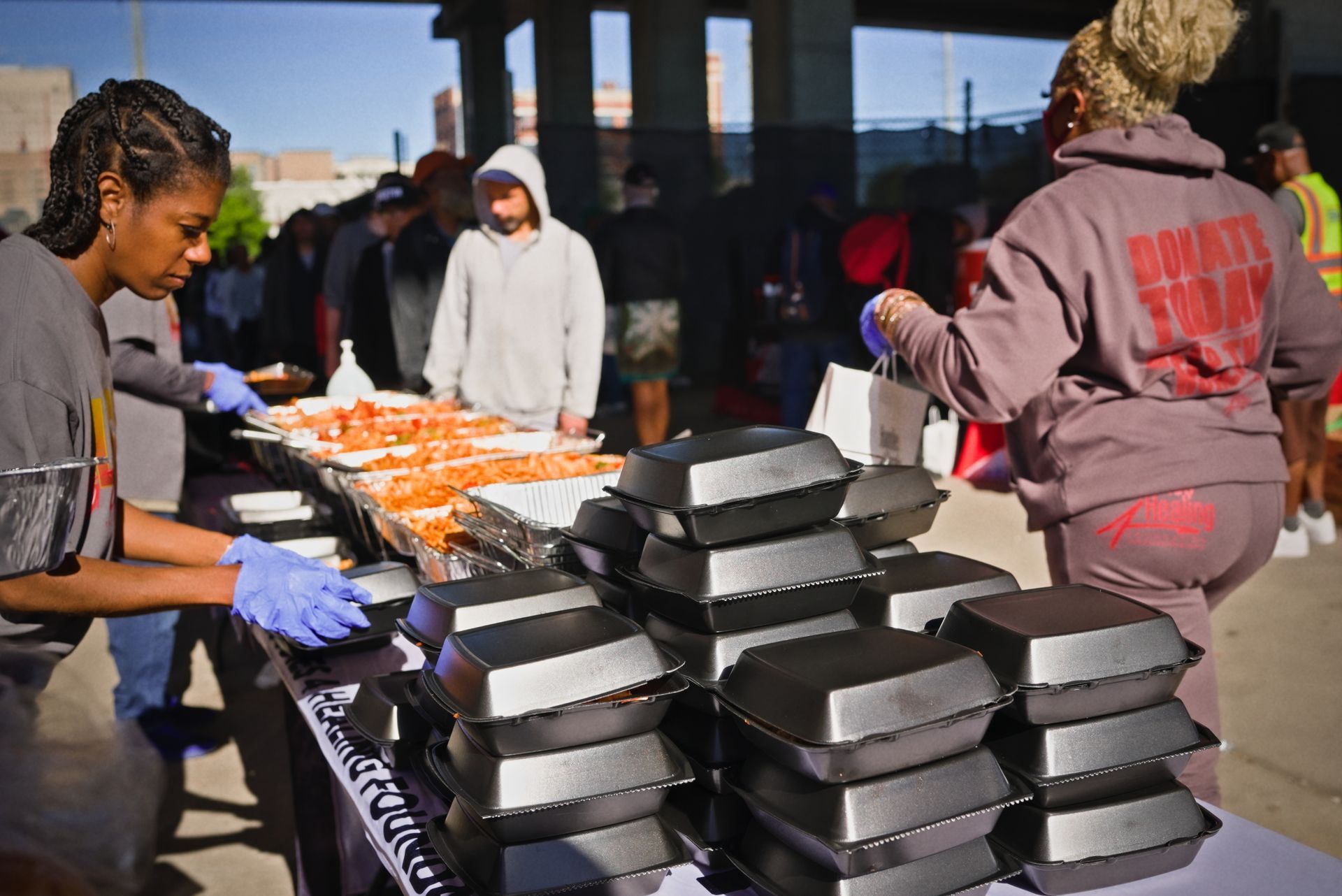A group of people are standing around a table with containers of food.