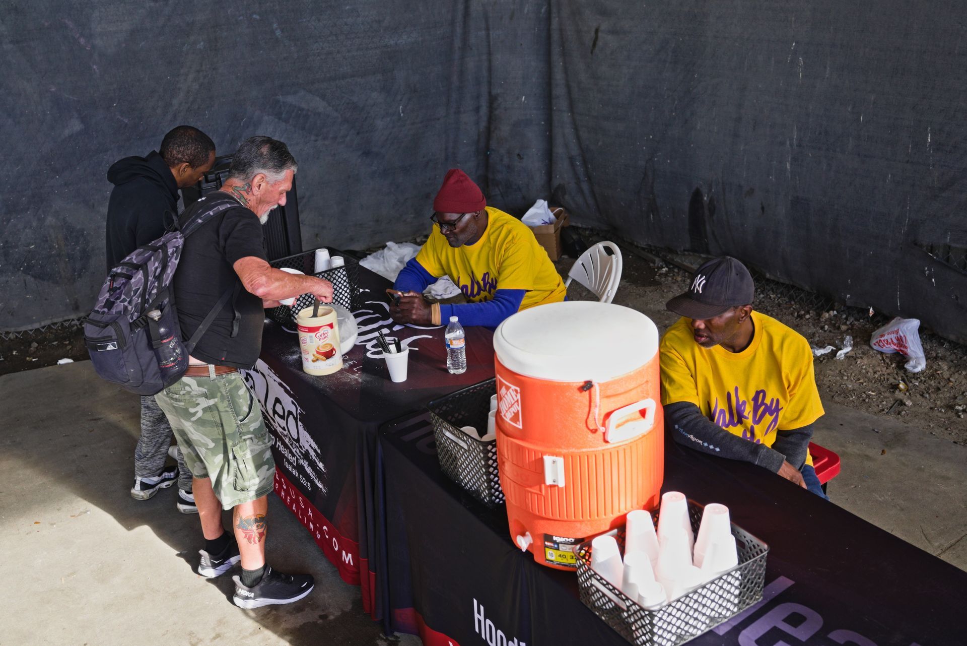 A group of people sitting around a table with a large orange cooler on it