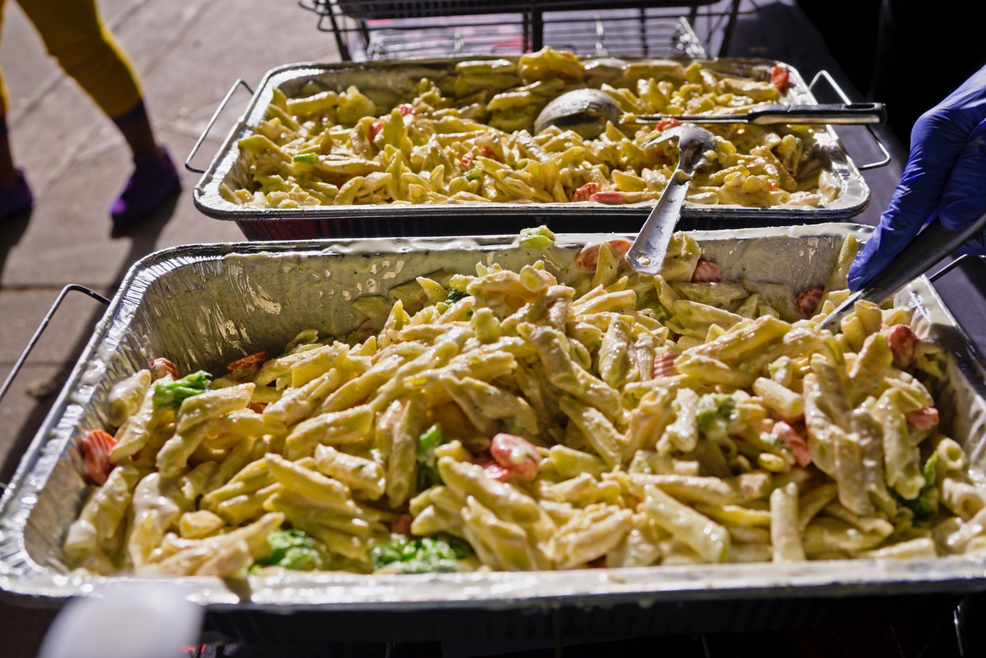 A tray of macaroni and cheese with vegetables and a spoon in it.