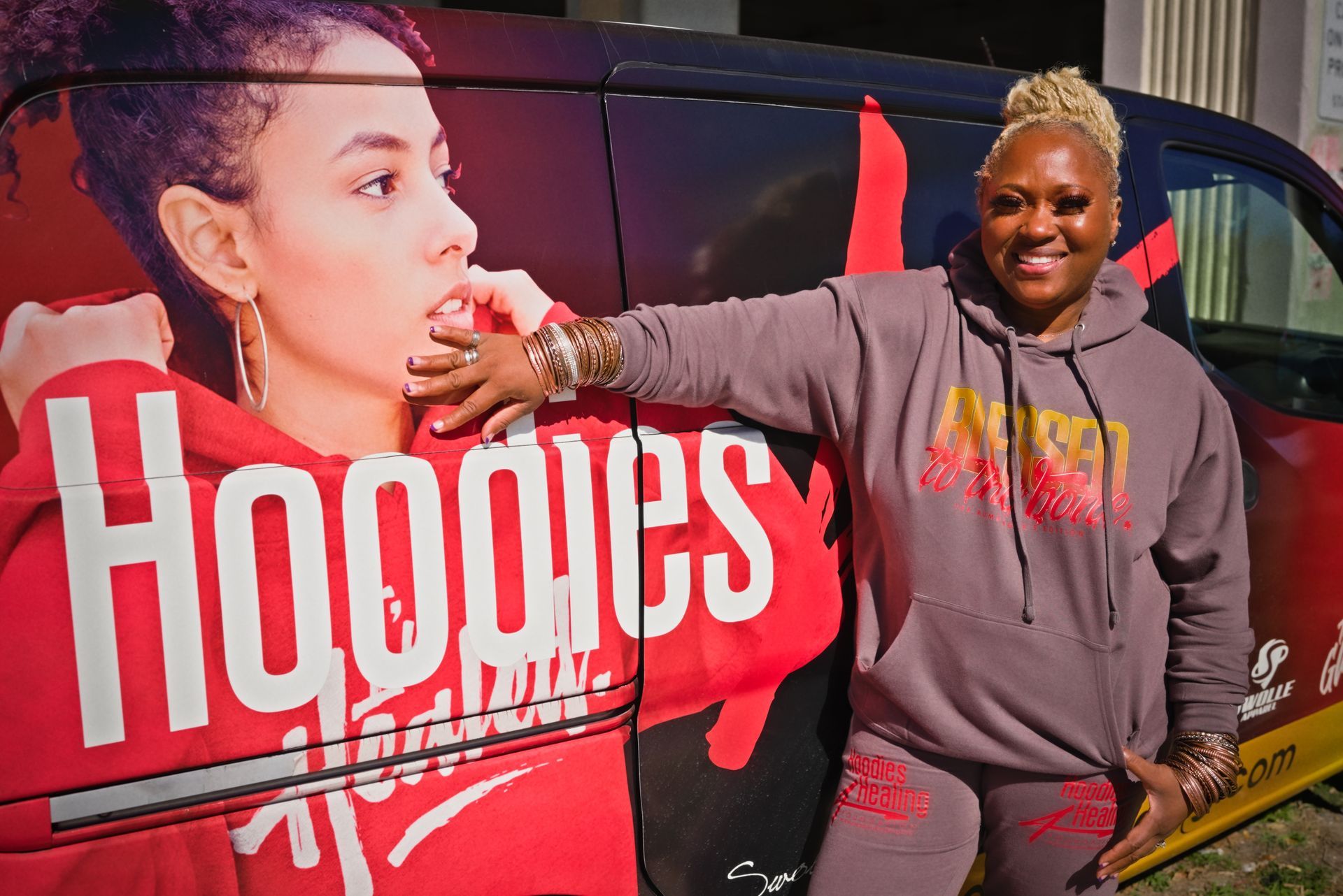 A woman in a hoodie is standing in front of a van that says hoodies.
