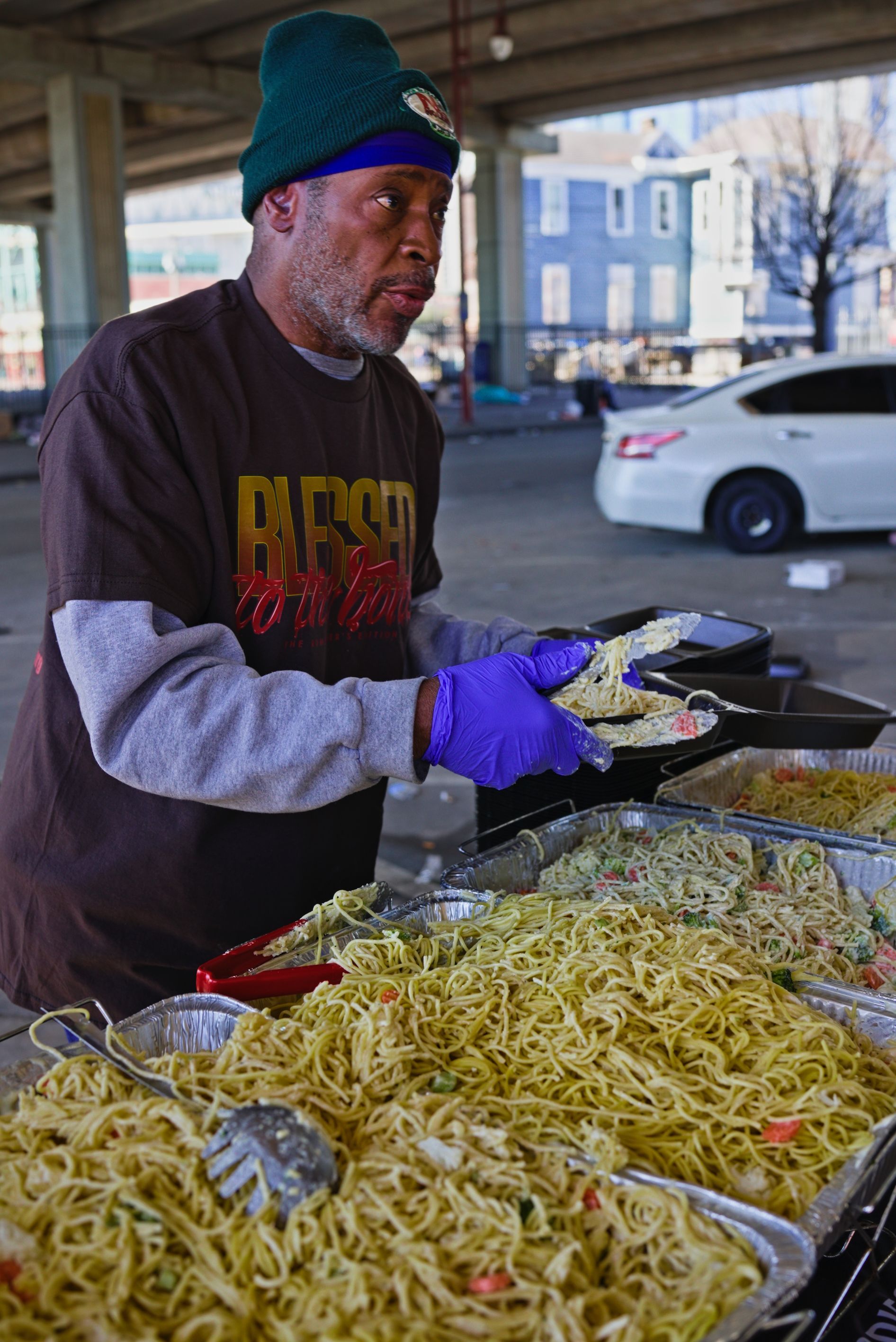 A man in purple gloves is serving noodles to a group of people.