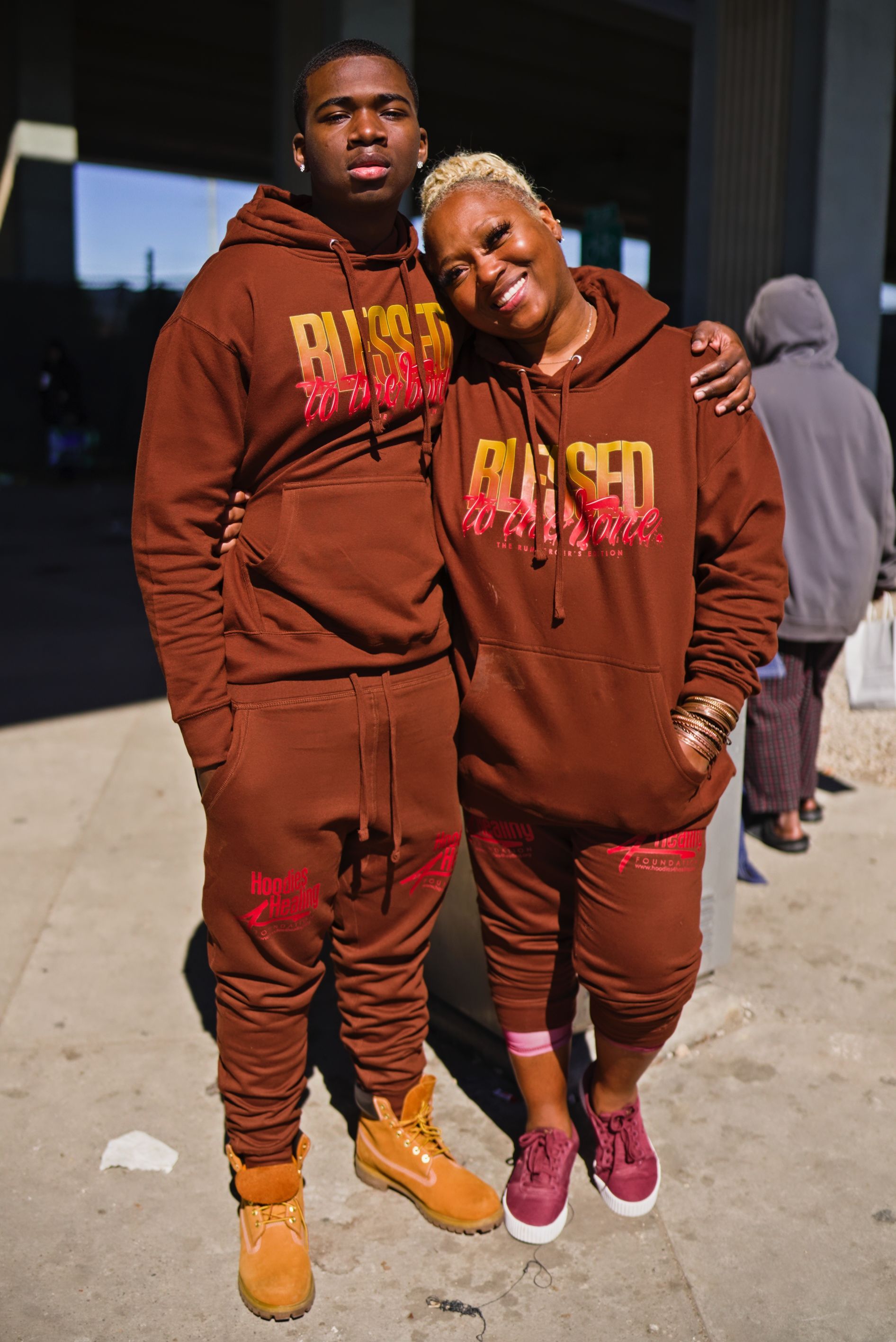A man and a woman are standing next to each other wearing brown hoodies.