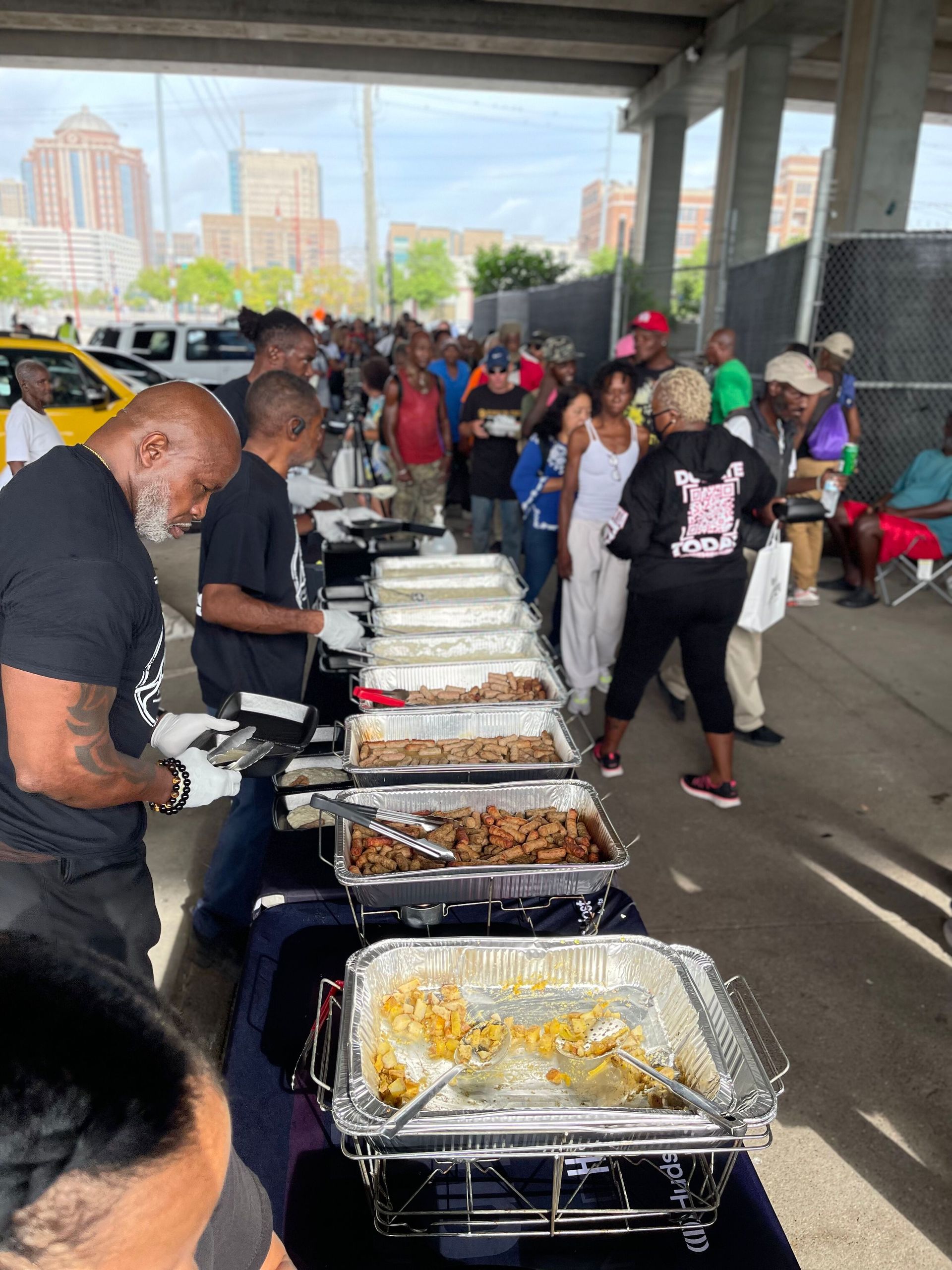 A group of people are standing around a table with trays of food.