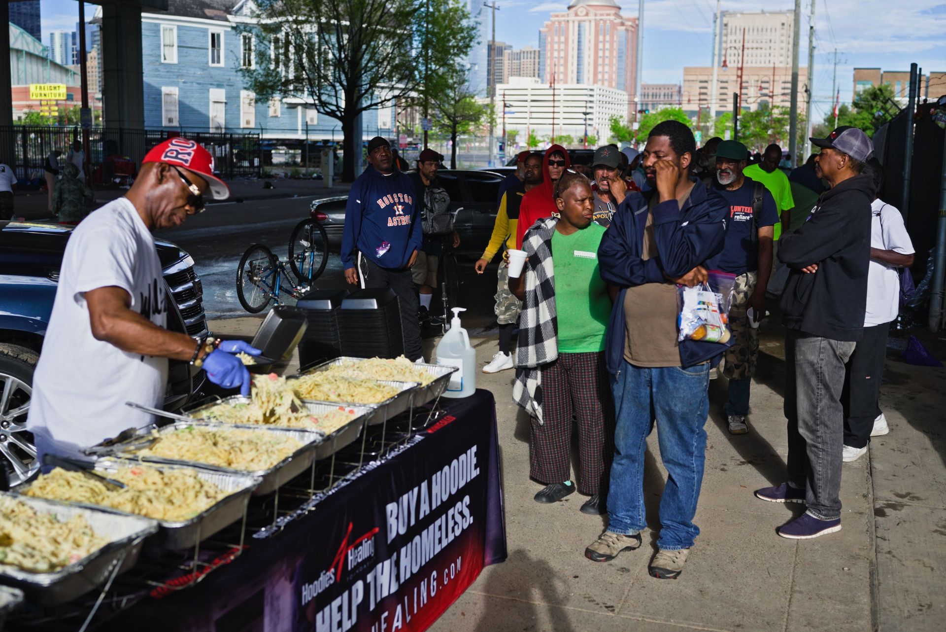 A group of people are standing around a table with food on it.