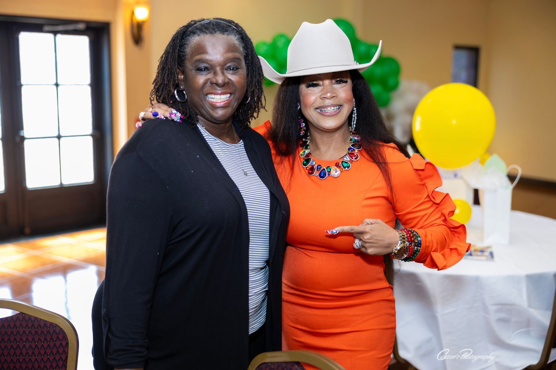 Two women are posing for a picture together in a room . one of the women is wearing a cowboy hat.