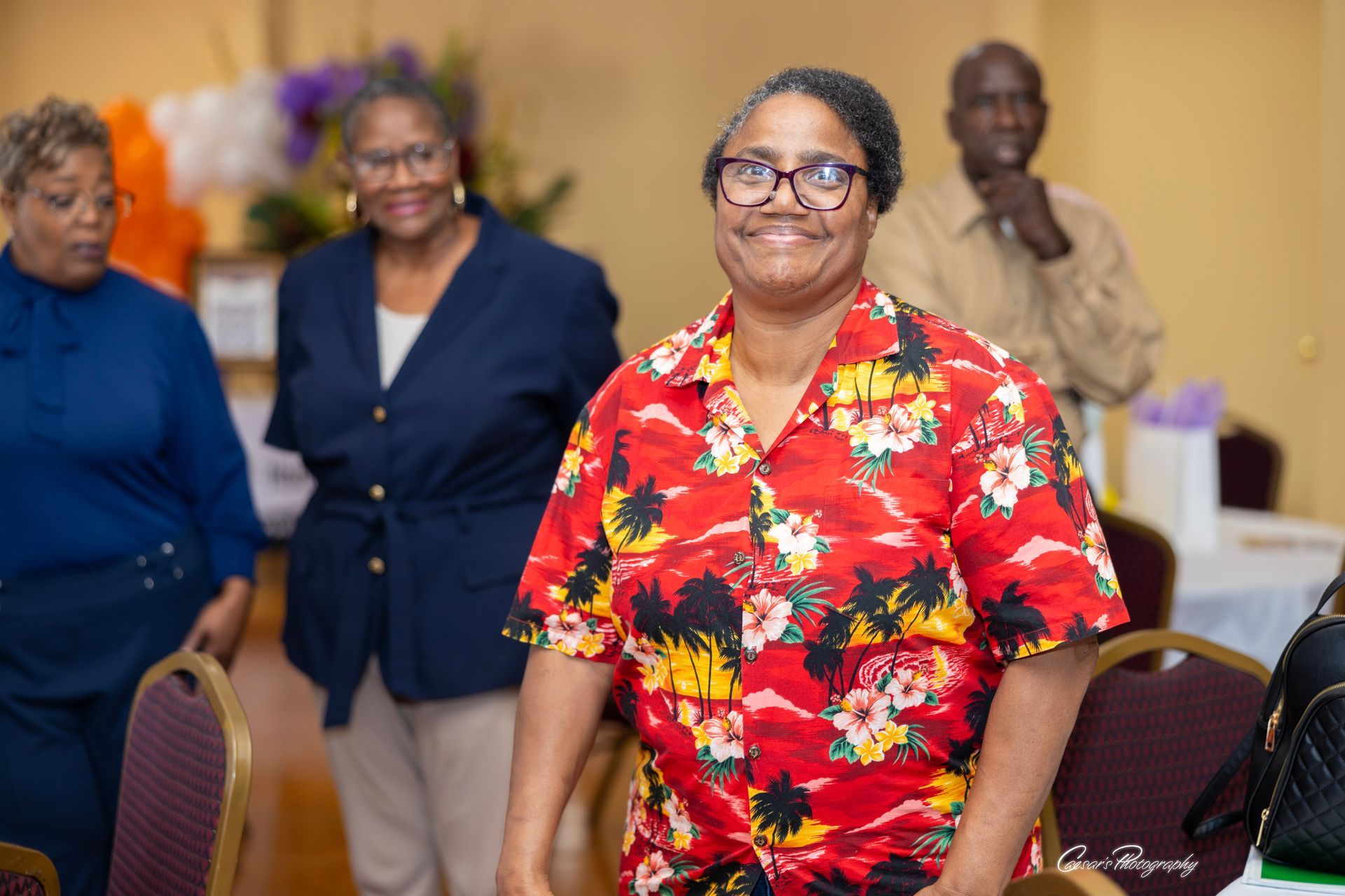 A woman in a red hawaiian shirt is standing in a room with other women.