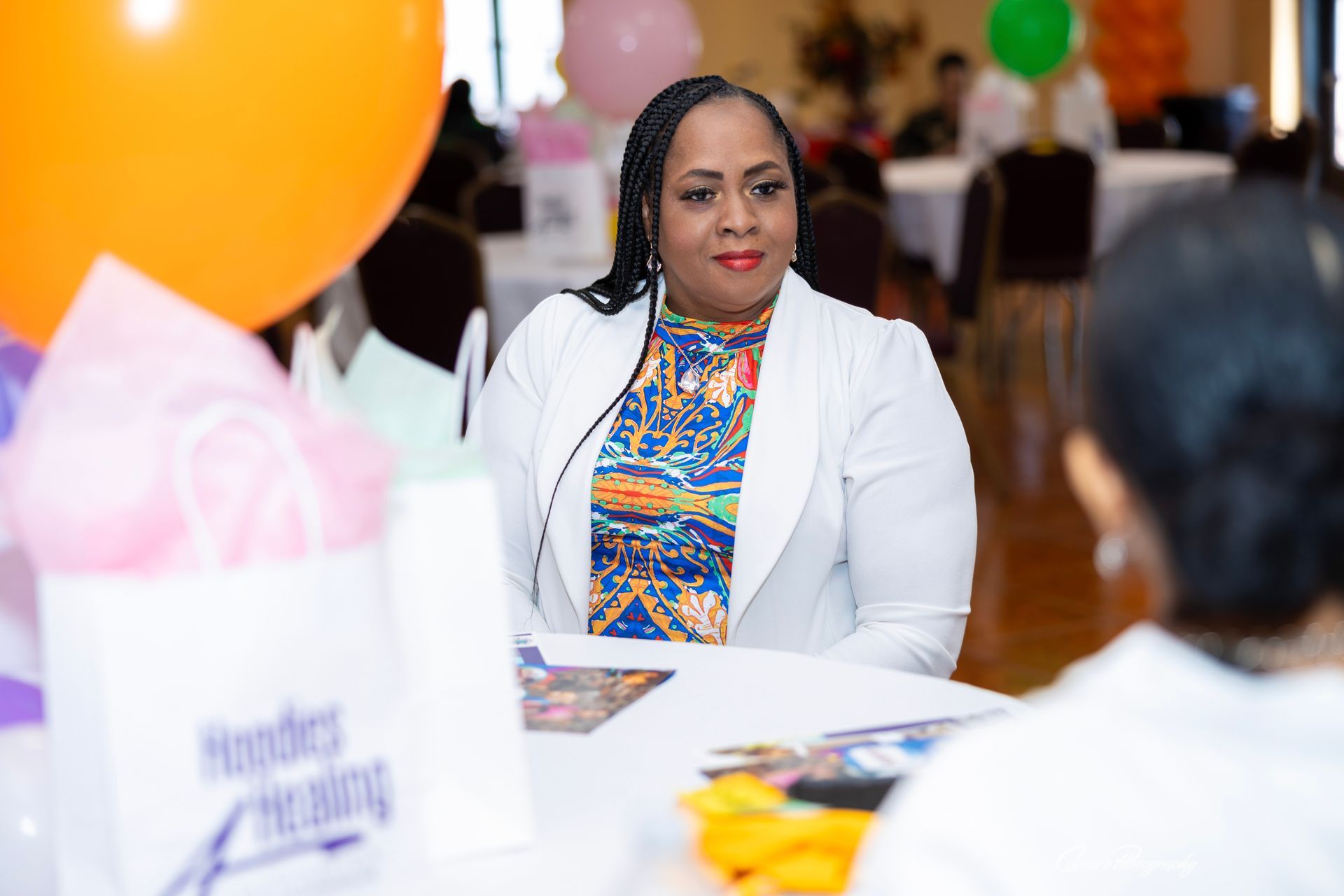 A woman is sitting at a table with balloons in the background.