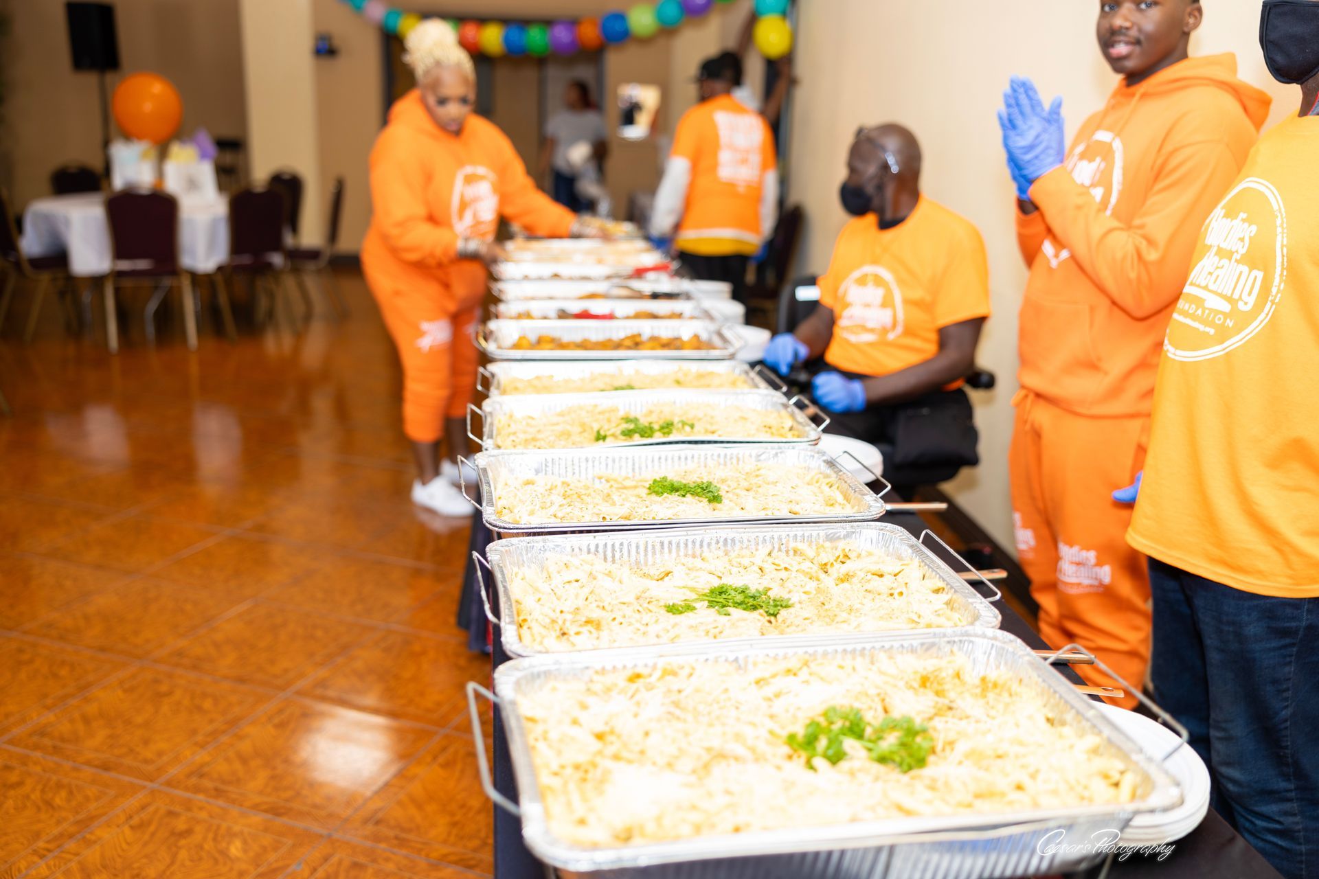 A group of people in orange shirts are serving food at a buffet table.