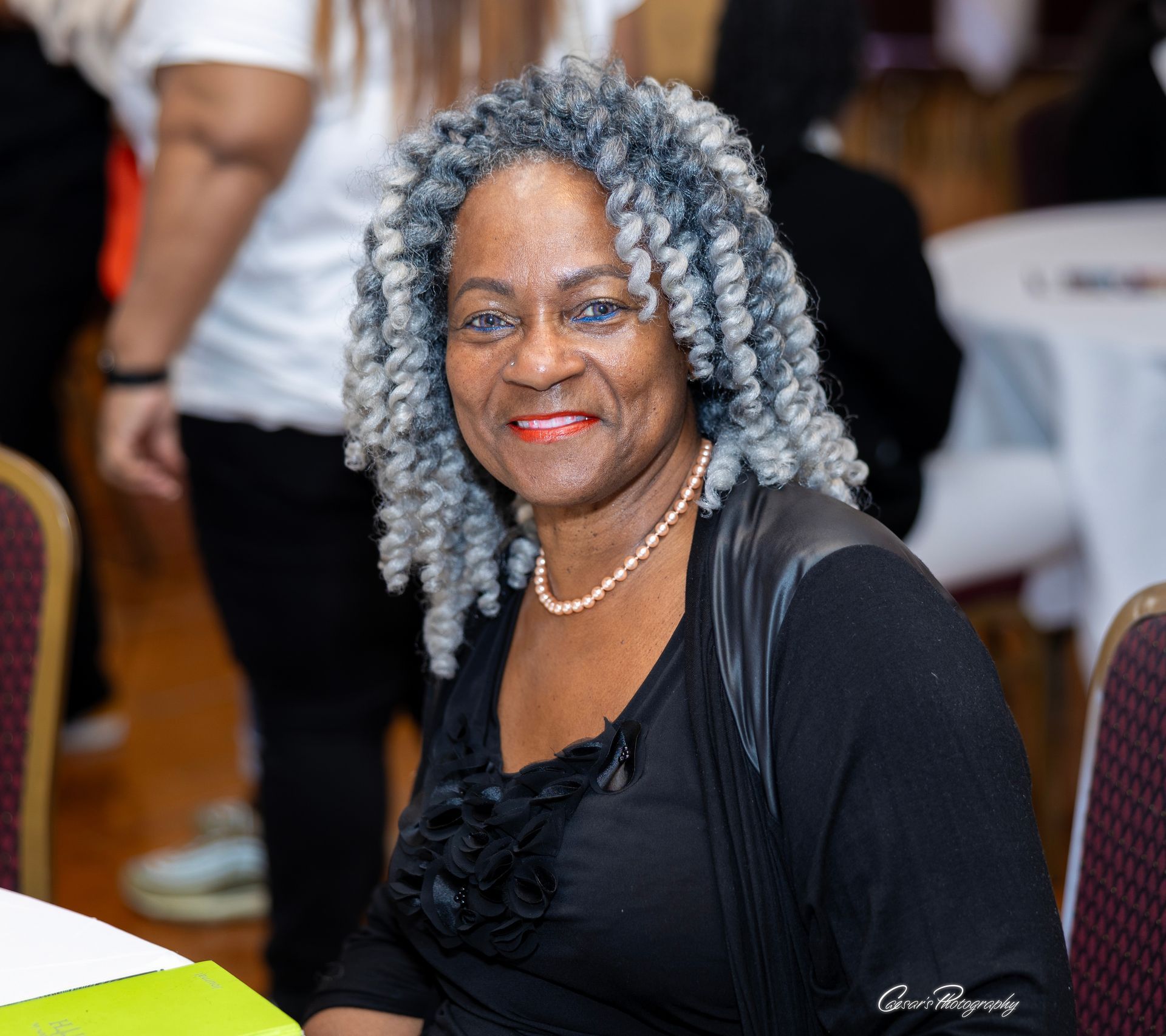 A woman with gray hair and a pearl necklace smiles for the camera
