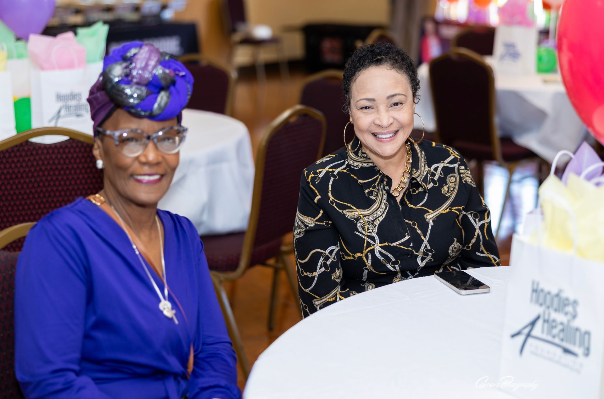 Two women are sitting at a table with balloons in the background.