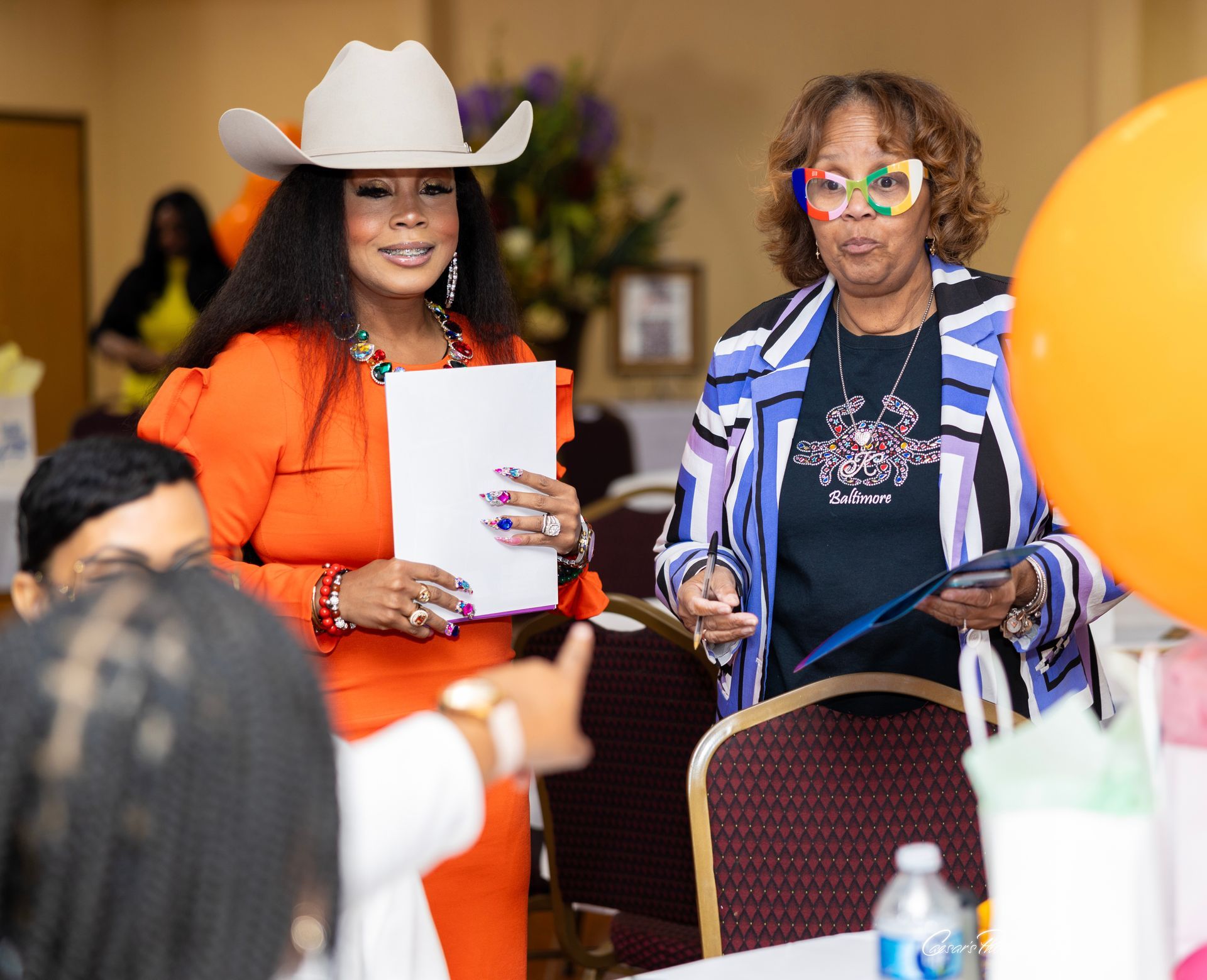 Two women are standing next to each other in a room holding papers.