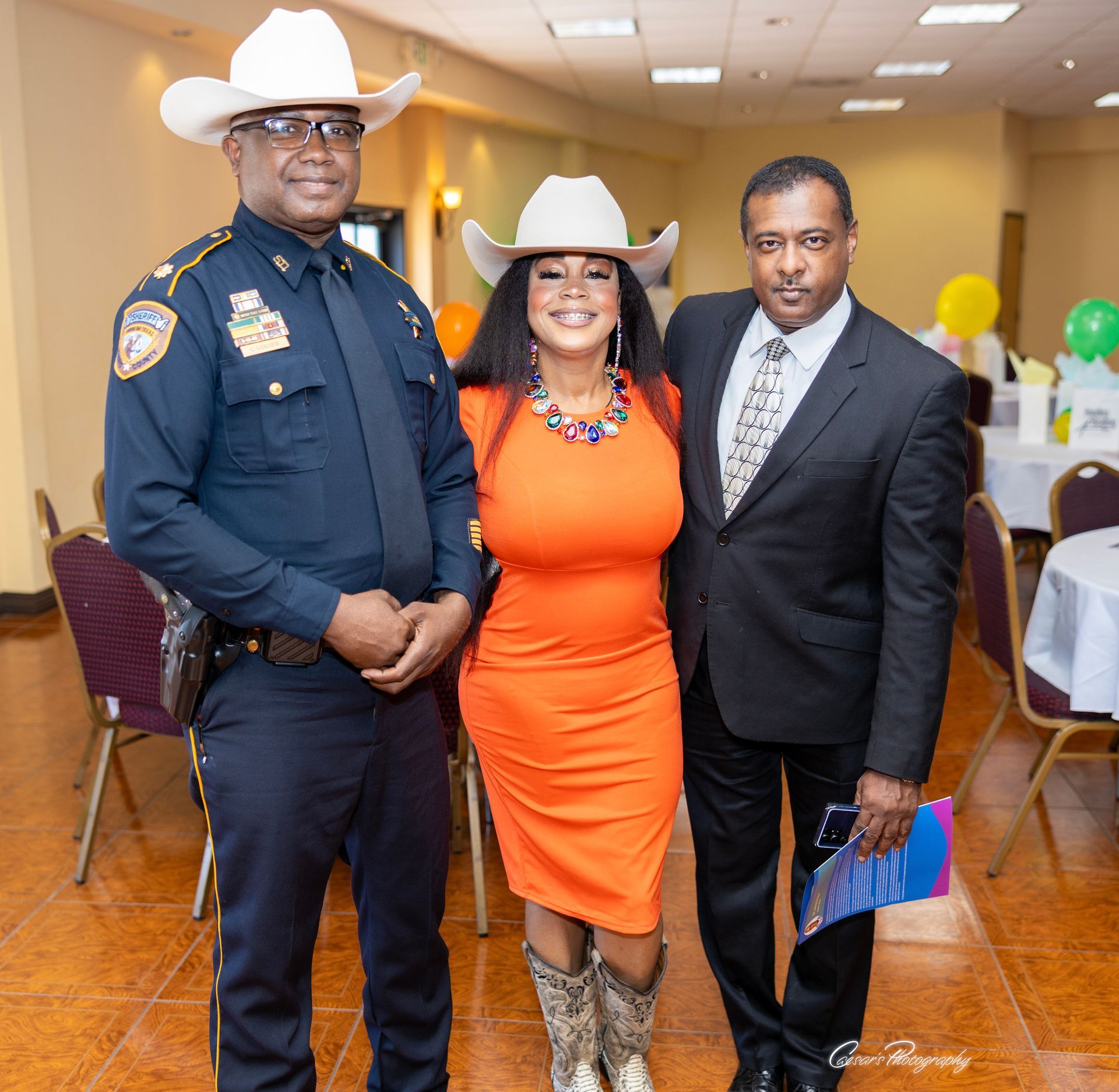 A woman in an orange dress is posing for a picture with two men in suits and cowboy hats