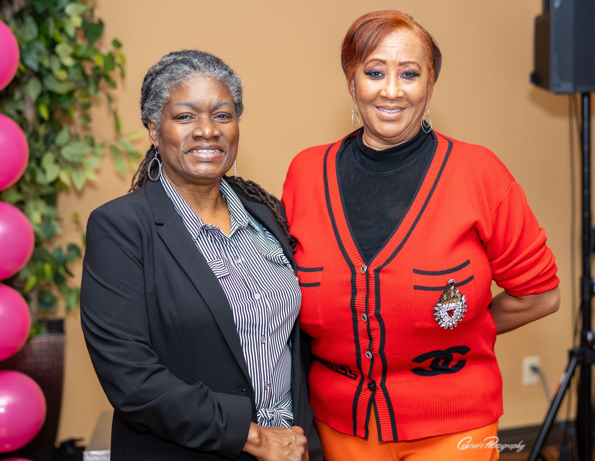 Two women are posing for a picture together in front of pink balloons.
