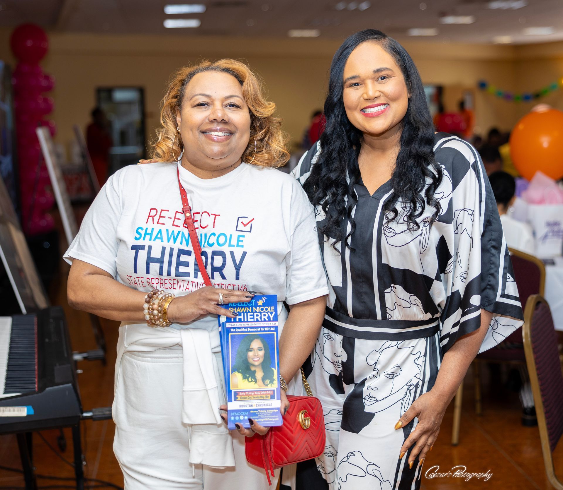 Two women are posing for a picture at a party . one of the women is holding a book.