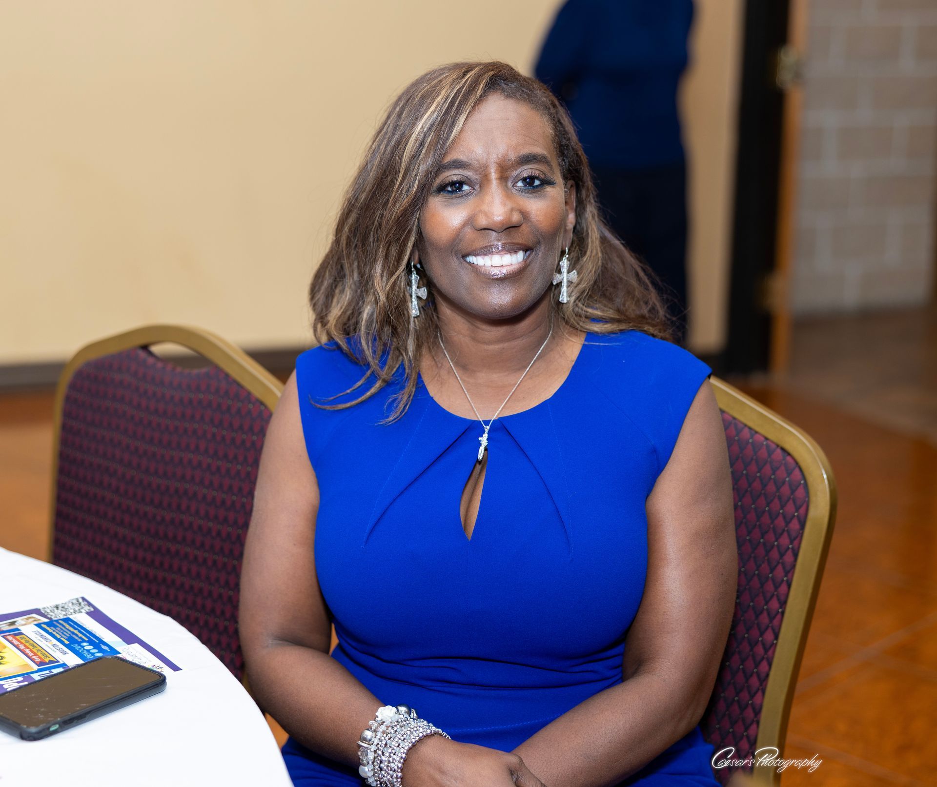 A woman in a blue dress is sitting at a table and smiling.