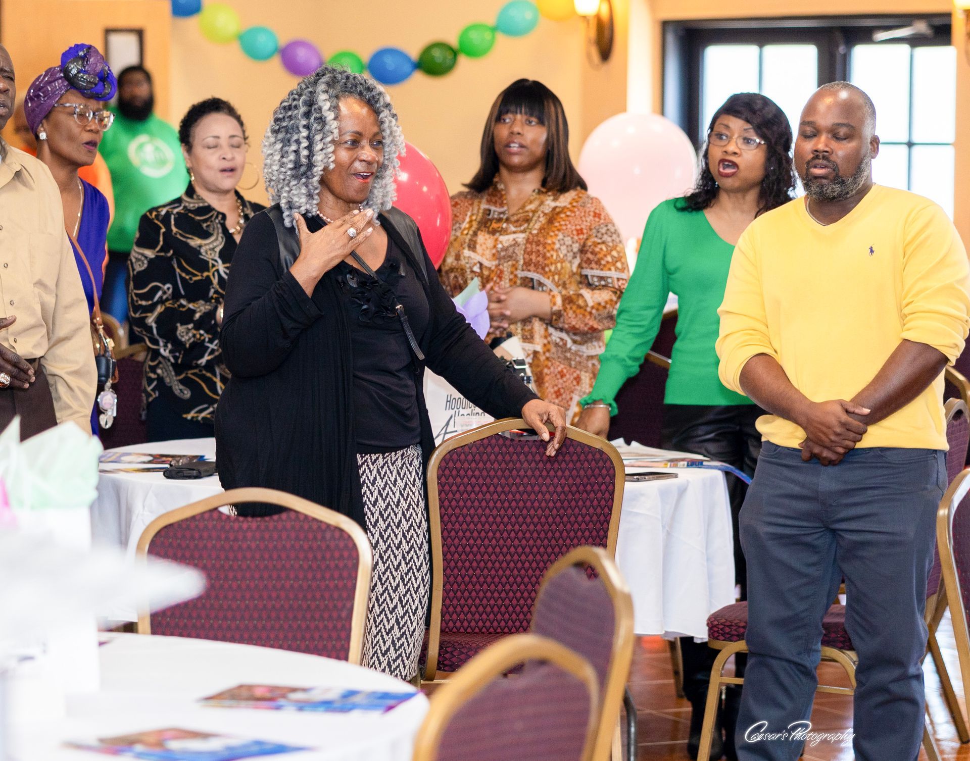 A group of people are standing around tables and chairs in a room.