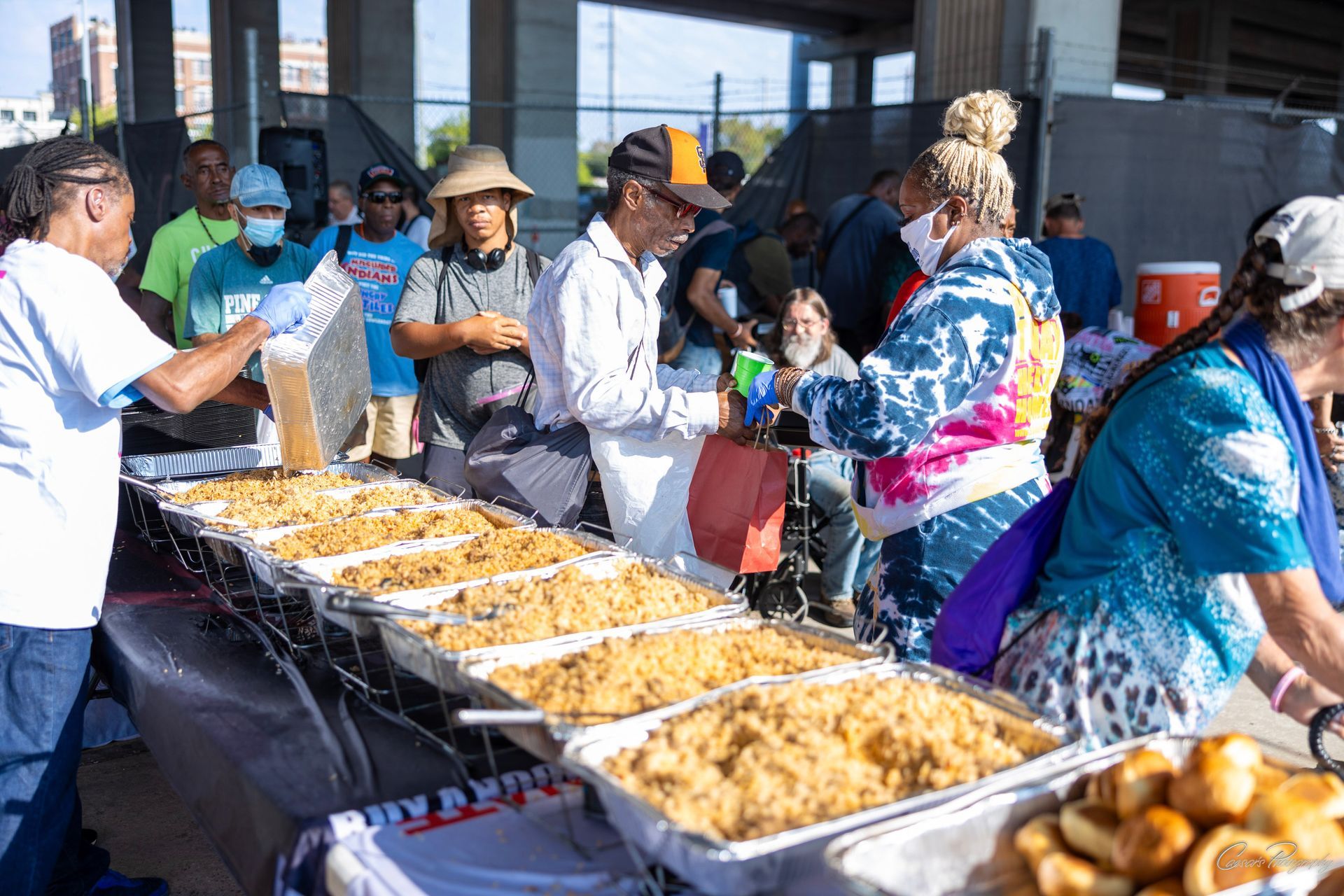 A group of people are standing around a table filled with plates of food.