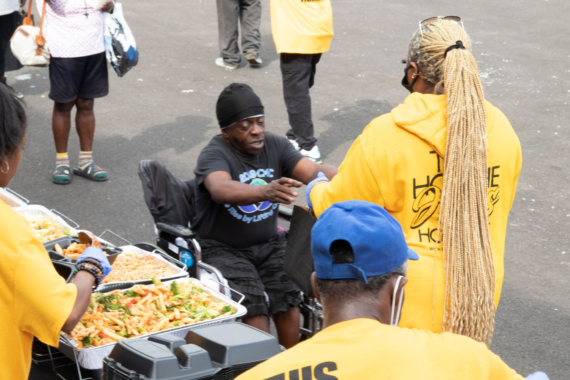 A man in a wheelchair is being served food by people in yellow shirts