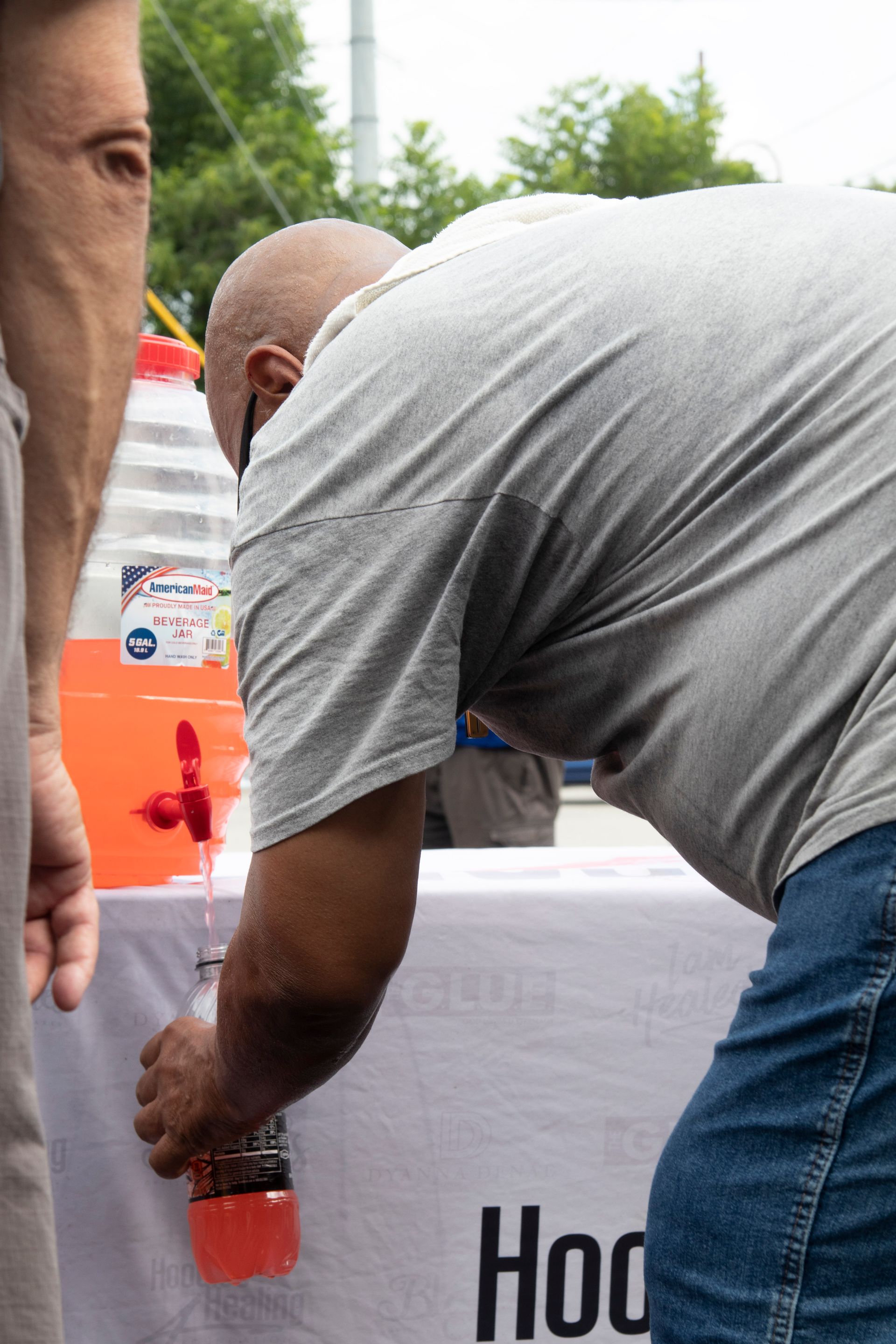 A man in a gray shirt is pouring liquid into a bottle.