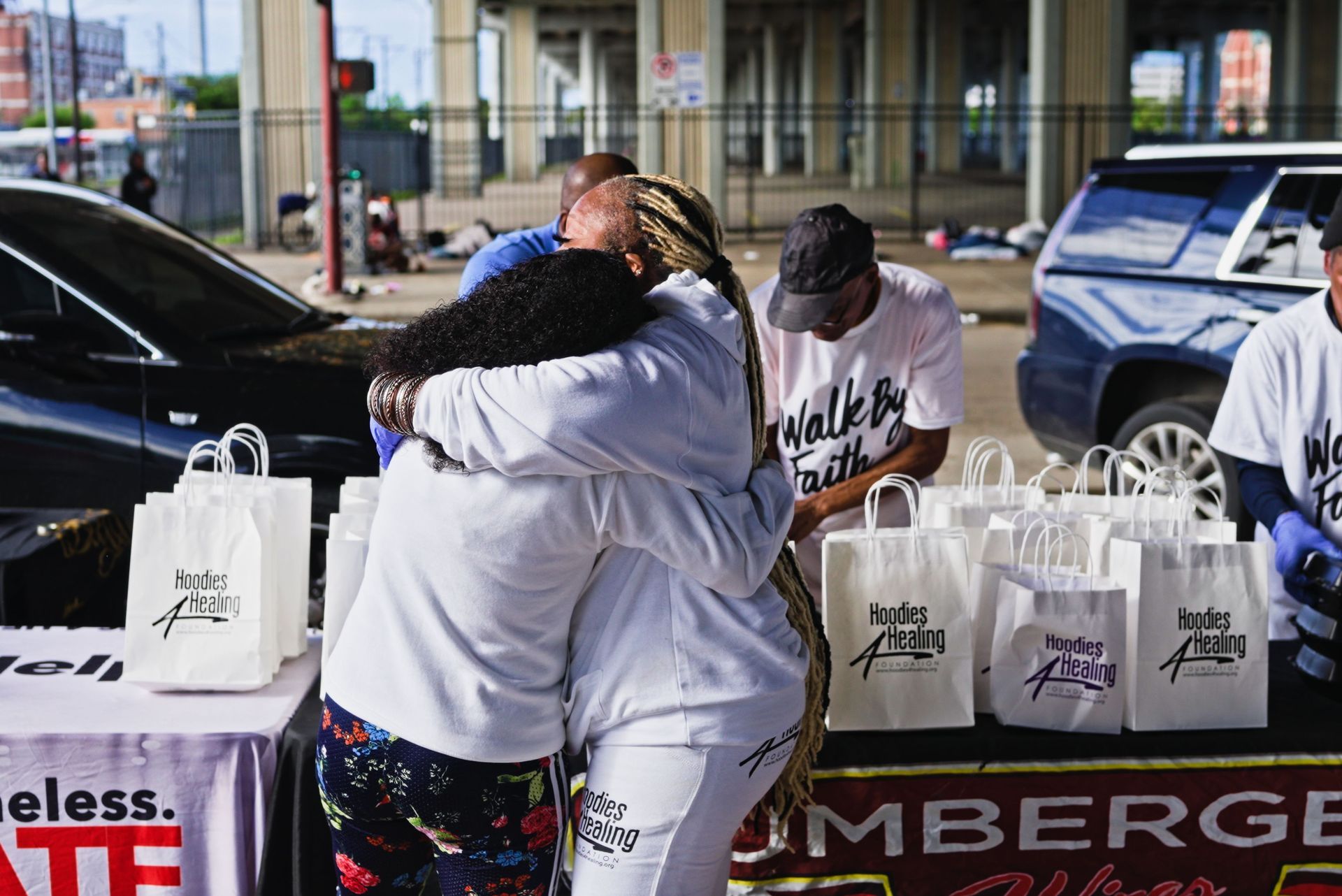 A group of people are hugging each other in front of a table with bags of food.