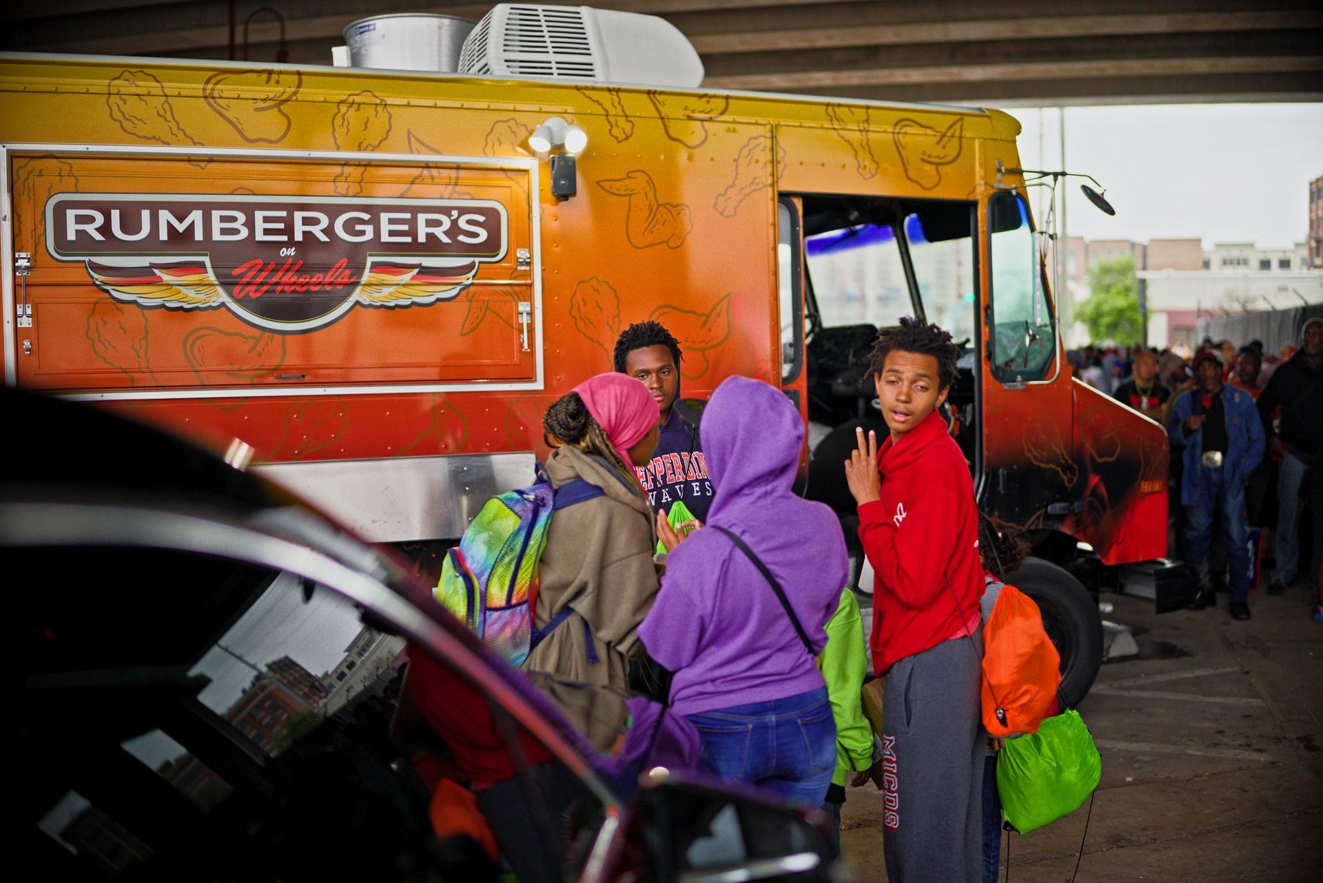 A group of people standing in front of a rumberger 's food truck.