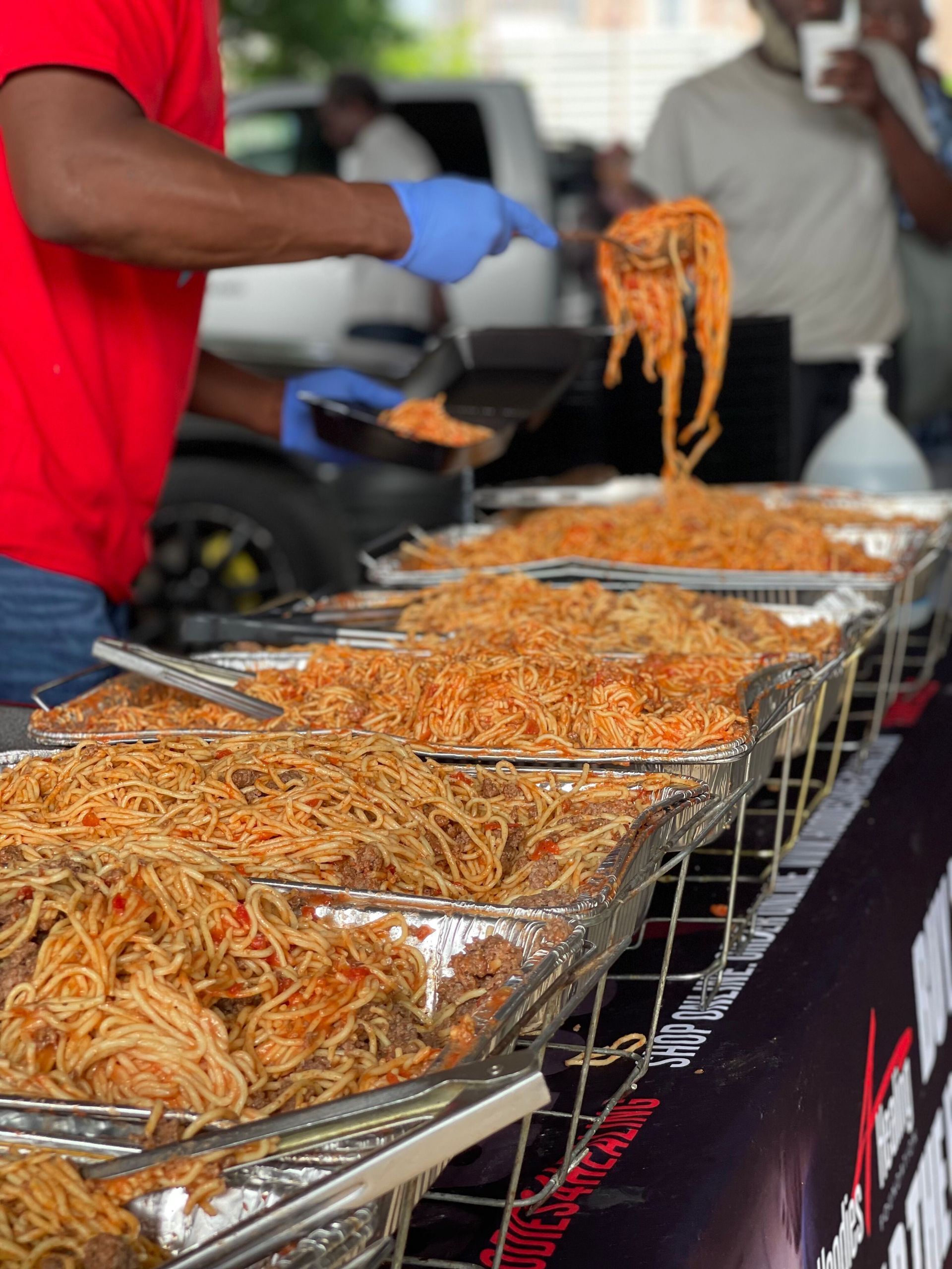 A man in a red shirt is serving noodles at a food stand.