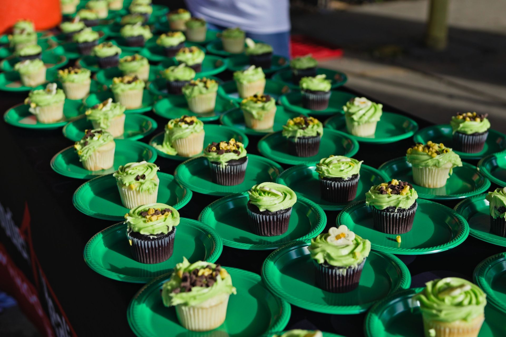 A bunch of cupcakes on green paper plates on a table.