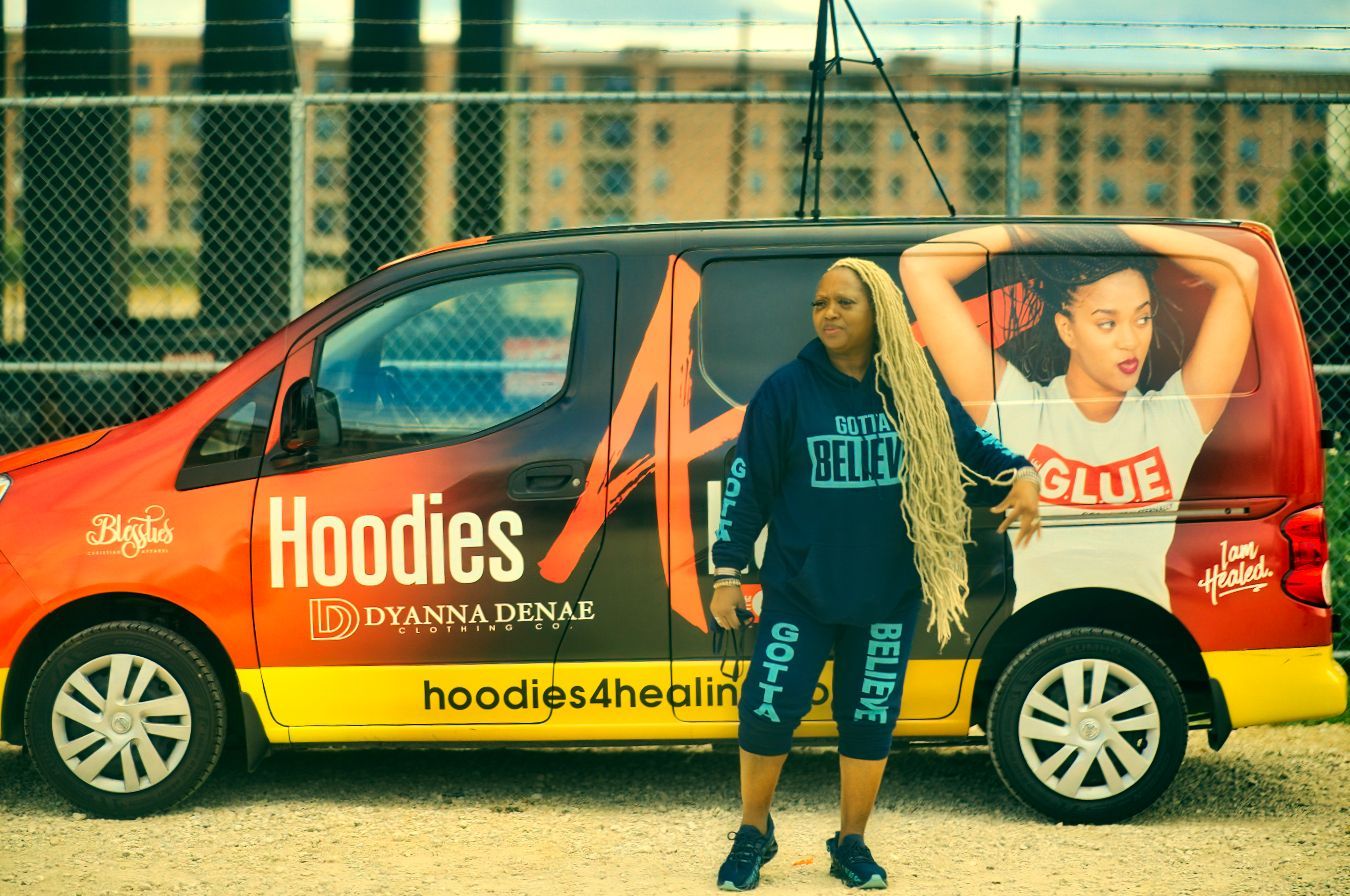A woman is standing in front of a van that says hoodies on it.