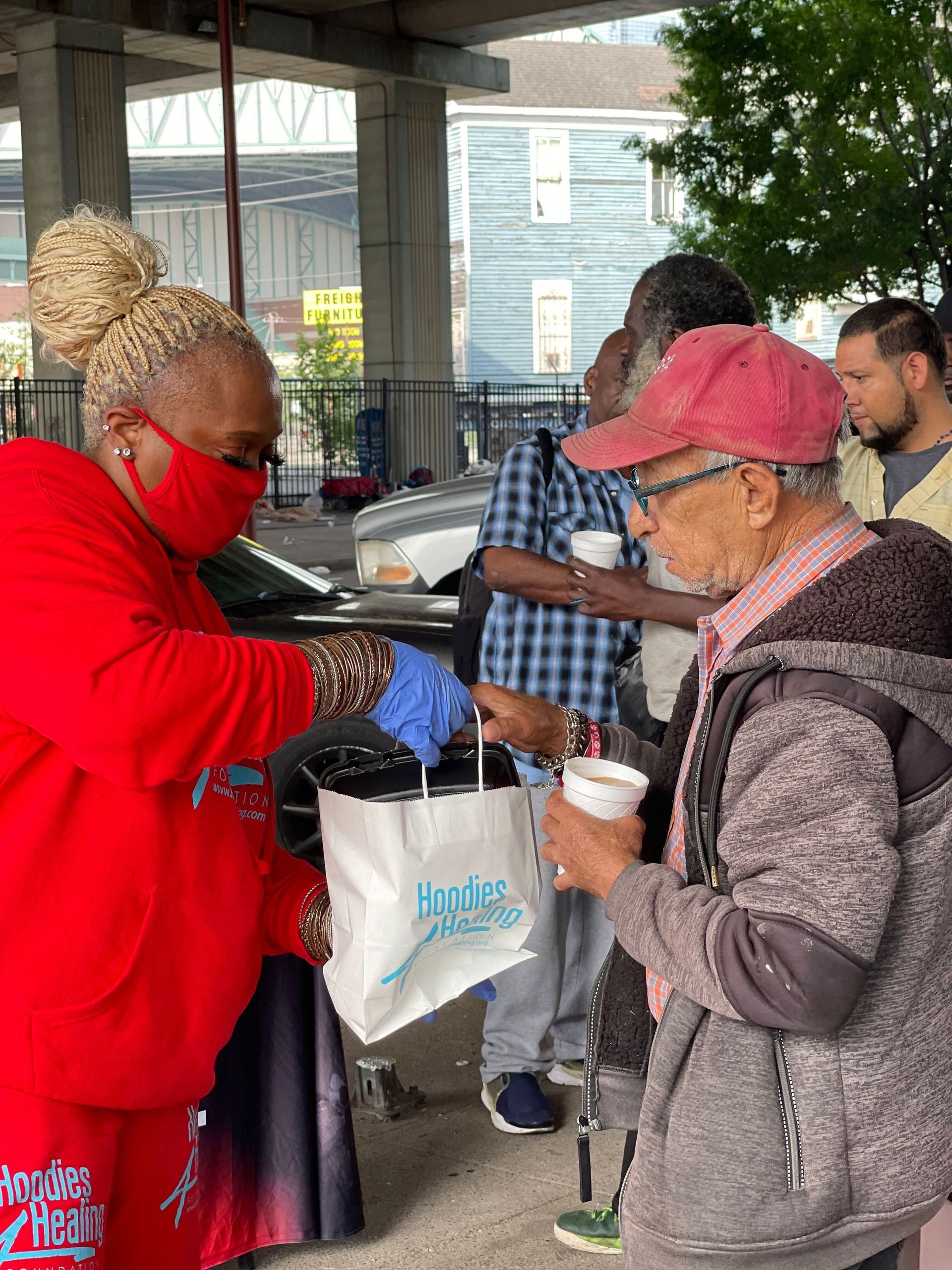 A woman wearing a red mask is giving food to a man.