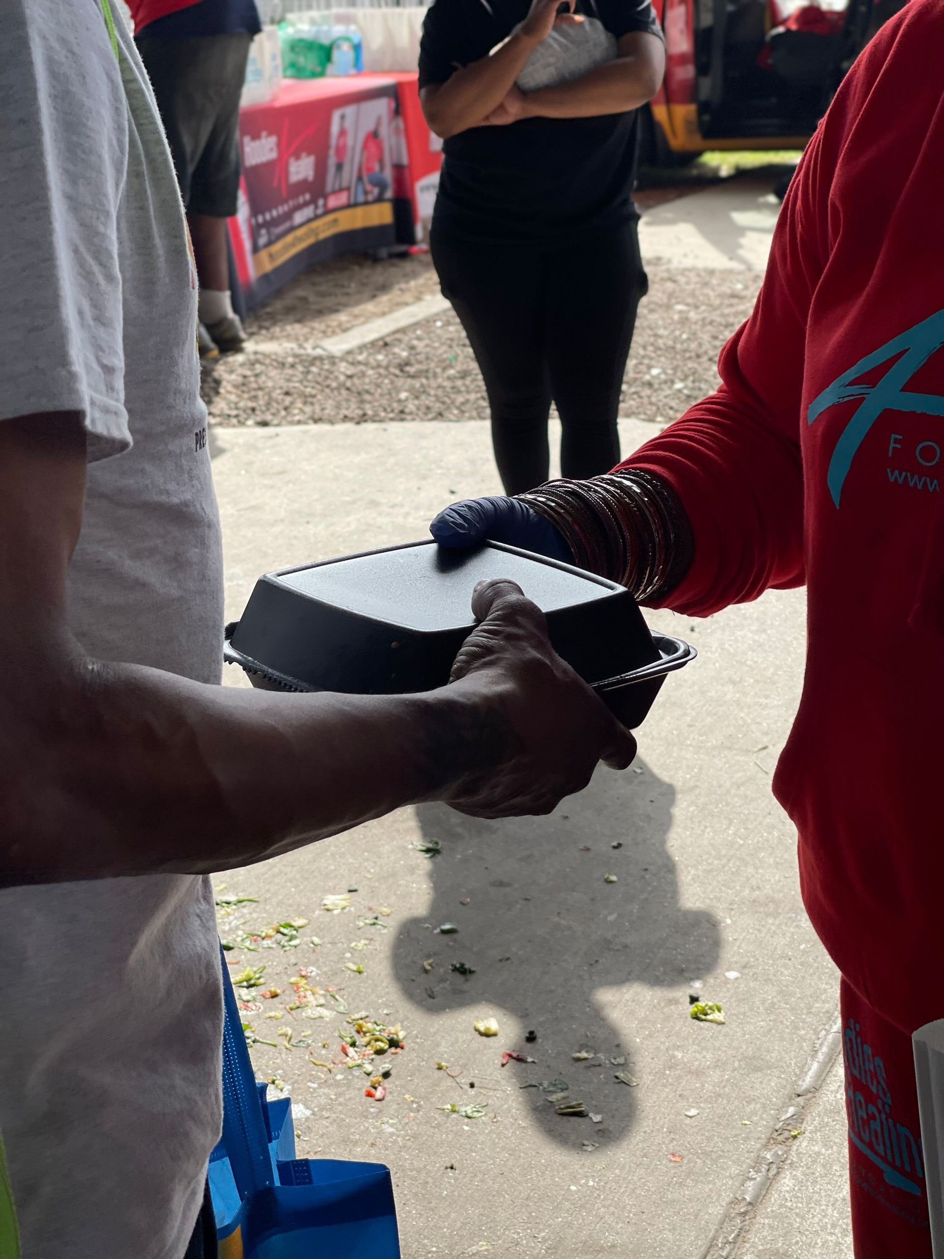 A woman in a red shirt is handing a container to a man